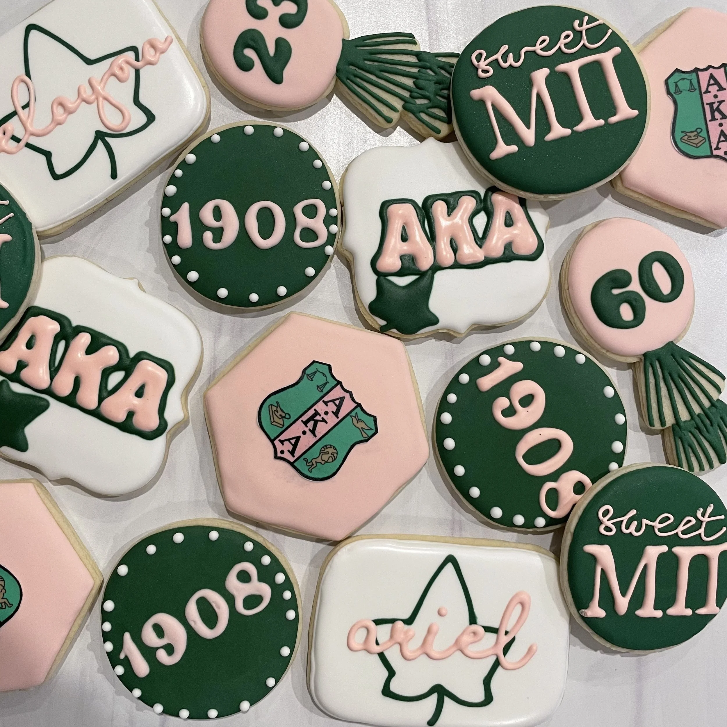 Decorative cookies with messages and symbols, including birthday and graduation themes, in pink, green, white, and black icing.