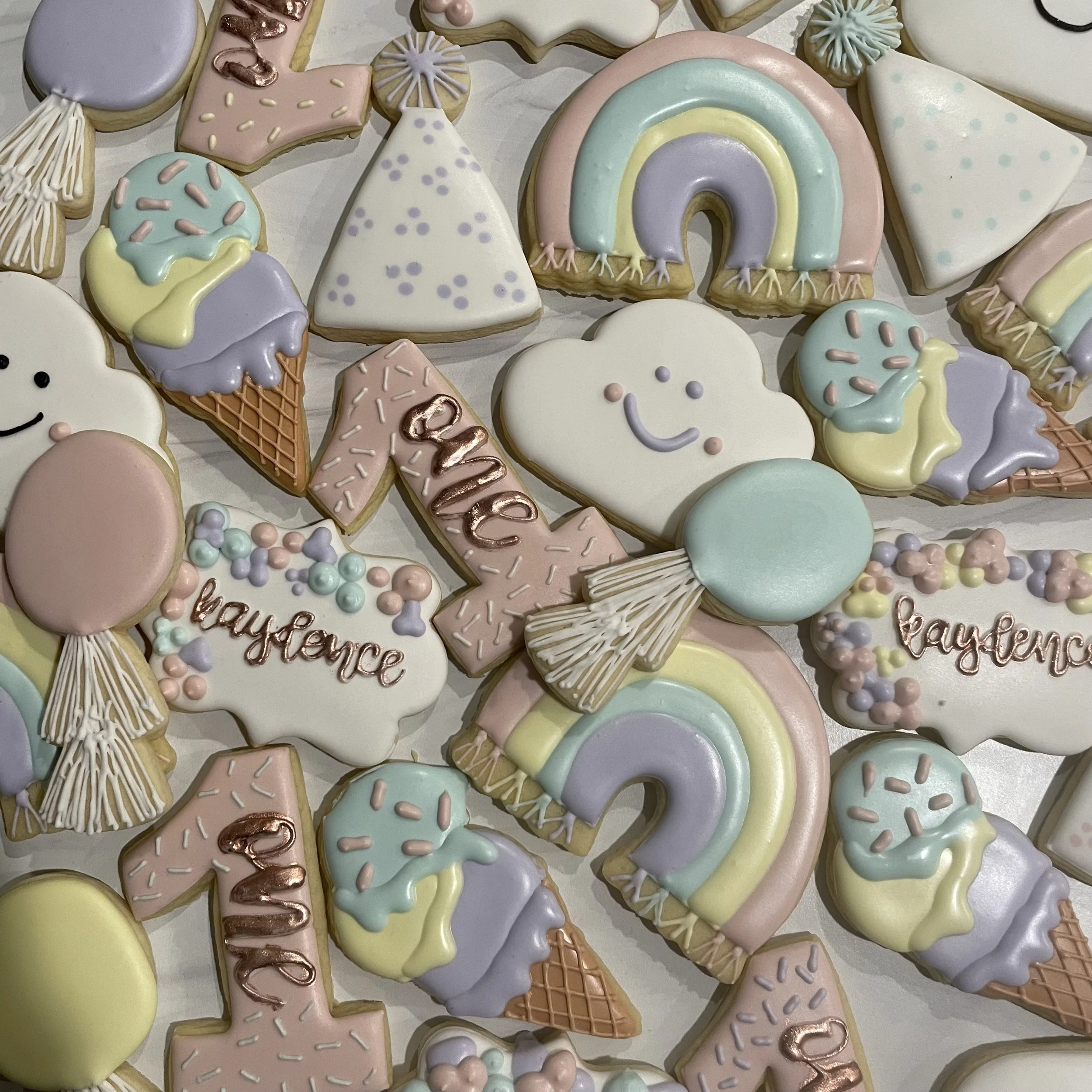 Colorful decorated cookies in various shapes, including rainbows, clouds, ice cream cones, stars, and hearts, decorated with pastel icing and sprinkles.