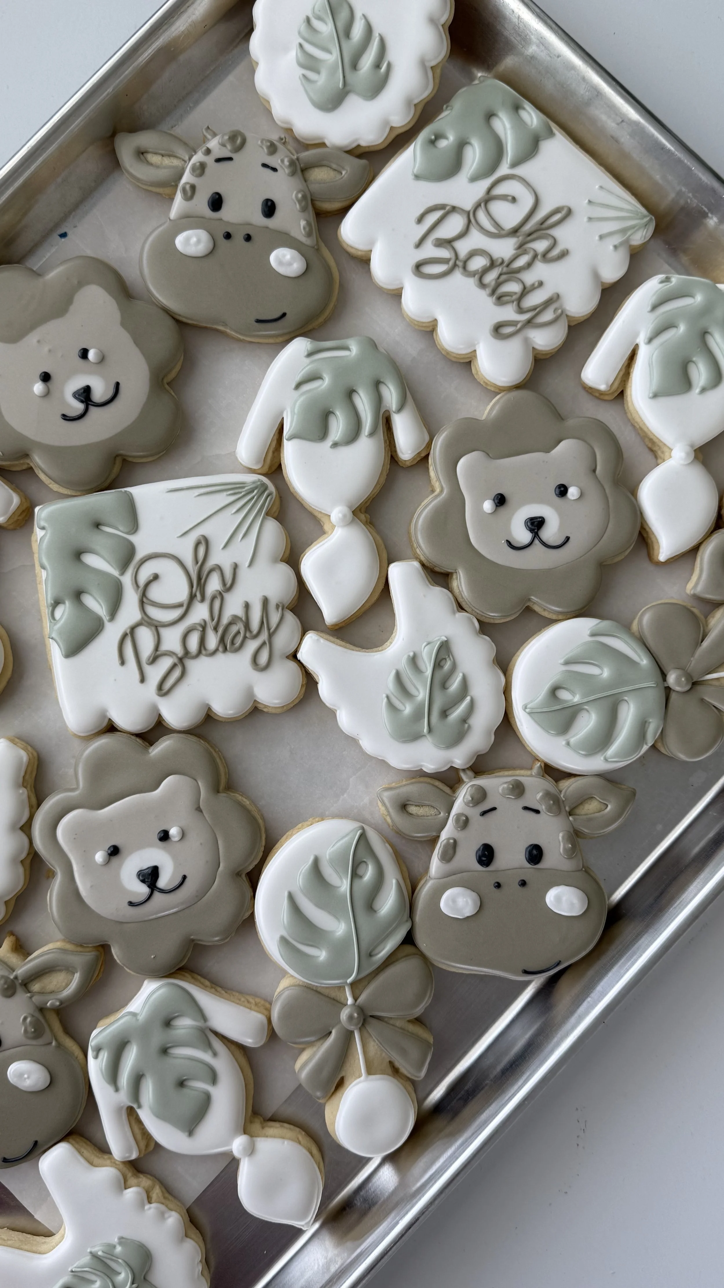 Cookies decorated with animal and botanical designs, including bears, giraffes, and leaves, some with 'Oh Baby' written on them.