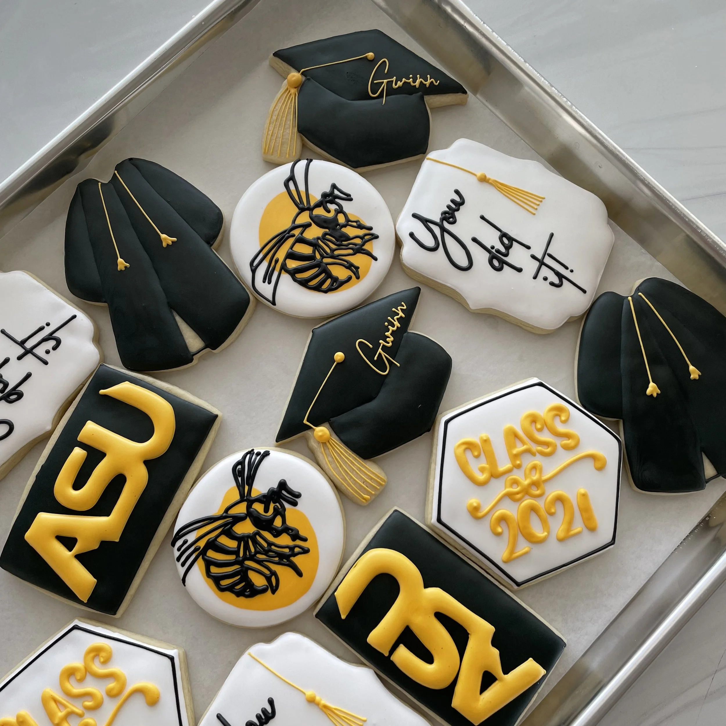 Decorated graduation cookies with black, white, and yellow icing, featuring cap and gown designs, a diploma, and the words 'Graduation' and 'Class of 2023'.