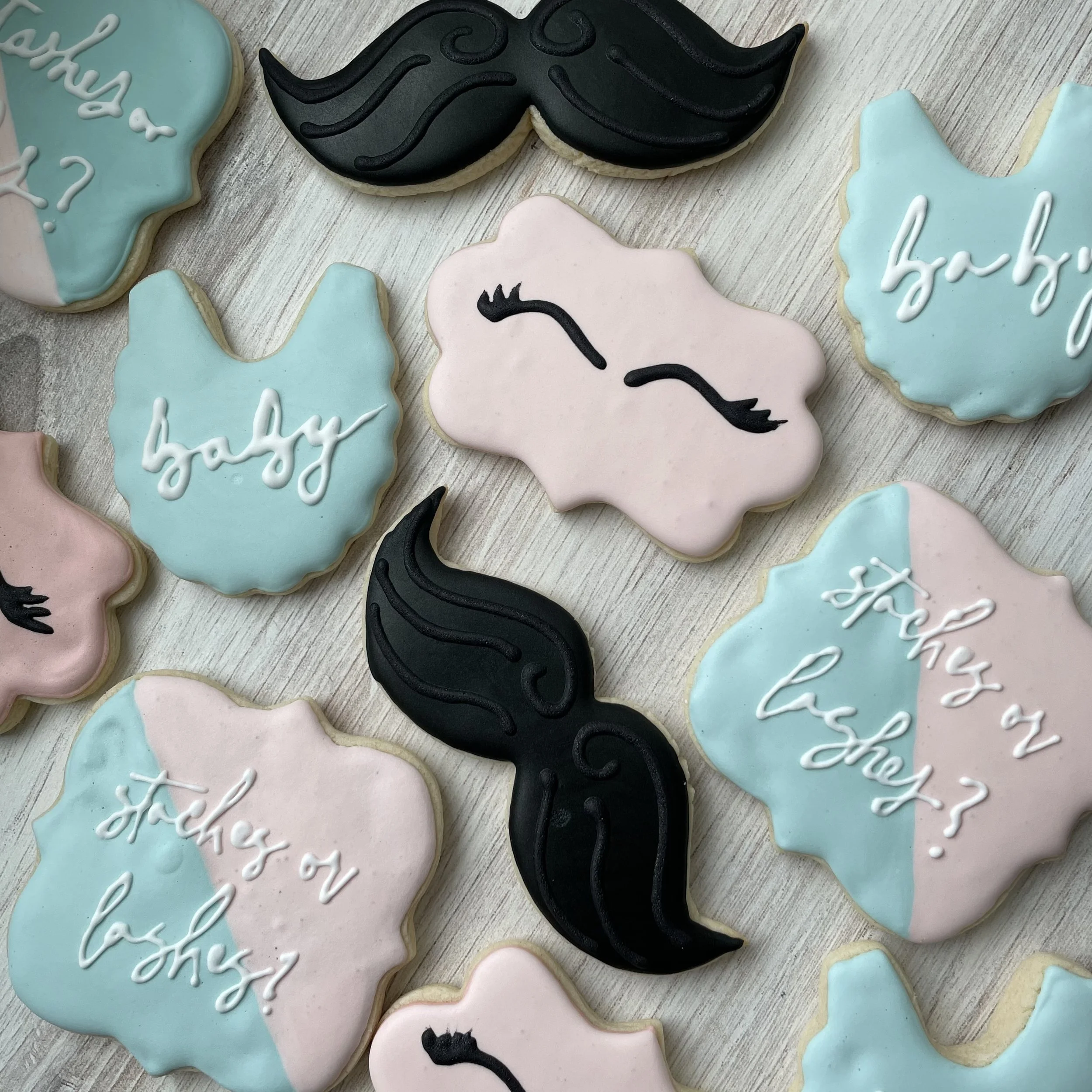Decorative cookies in the shape of unicorn heads with pastel pink, blue, and black icing, some featuring white text that says 'baby' and 'she'.