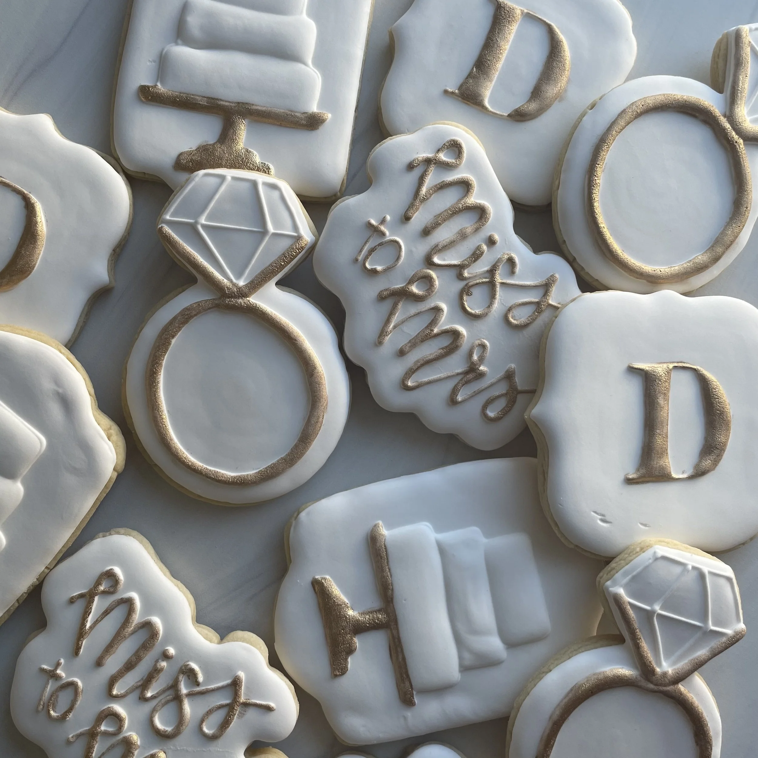 White decorated cookies with gold accents and cursive writing for a celebration.