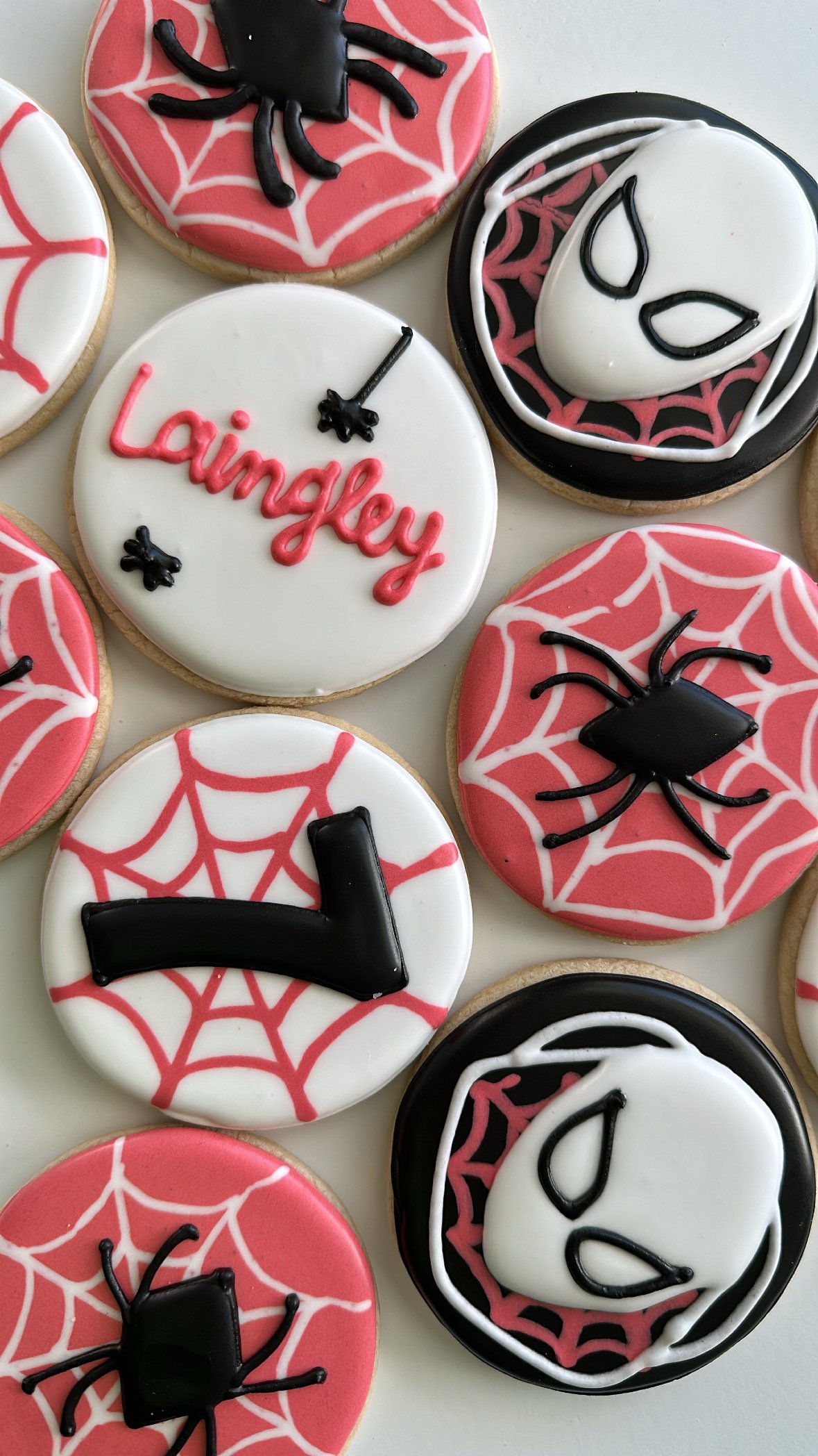 Decorated cookies with Halloween themes, including spider web designs, a spider, and a face mask, with one cookie featuring the name 'Laingley' and a small black spider.