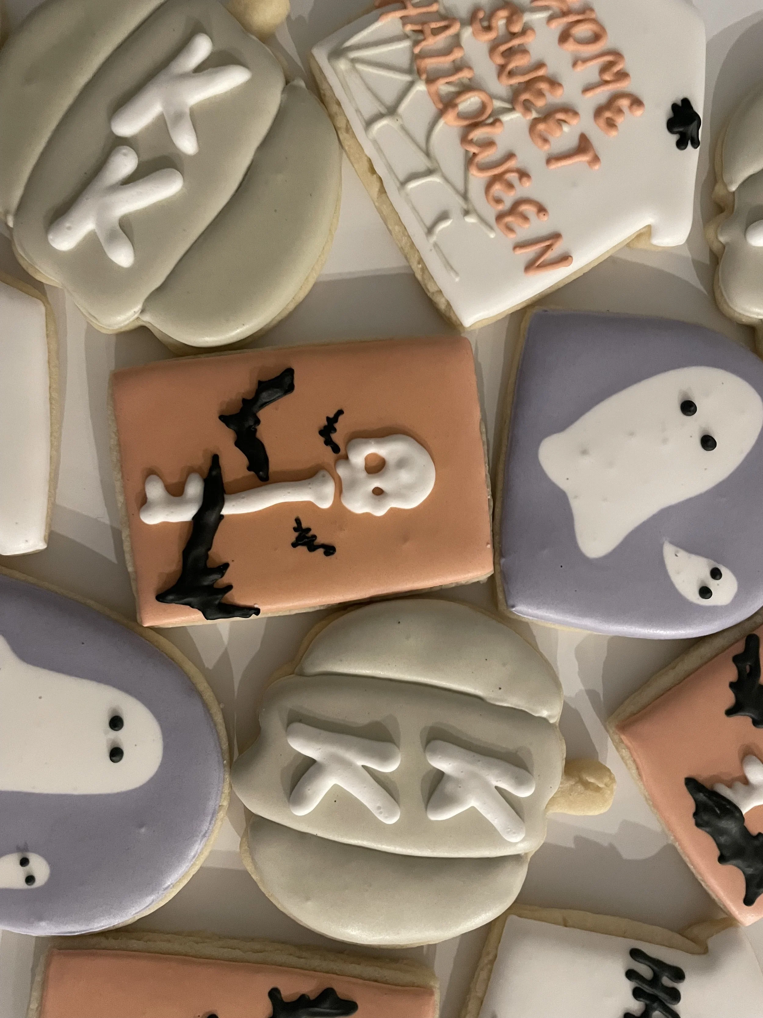 A collection of Halloween-themed sugar cookies decorated with icing and black candy accents, featuring ghost, pumpkin, and 'Trick or Treat' designs.