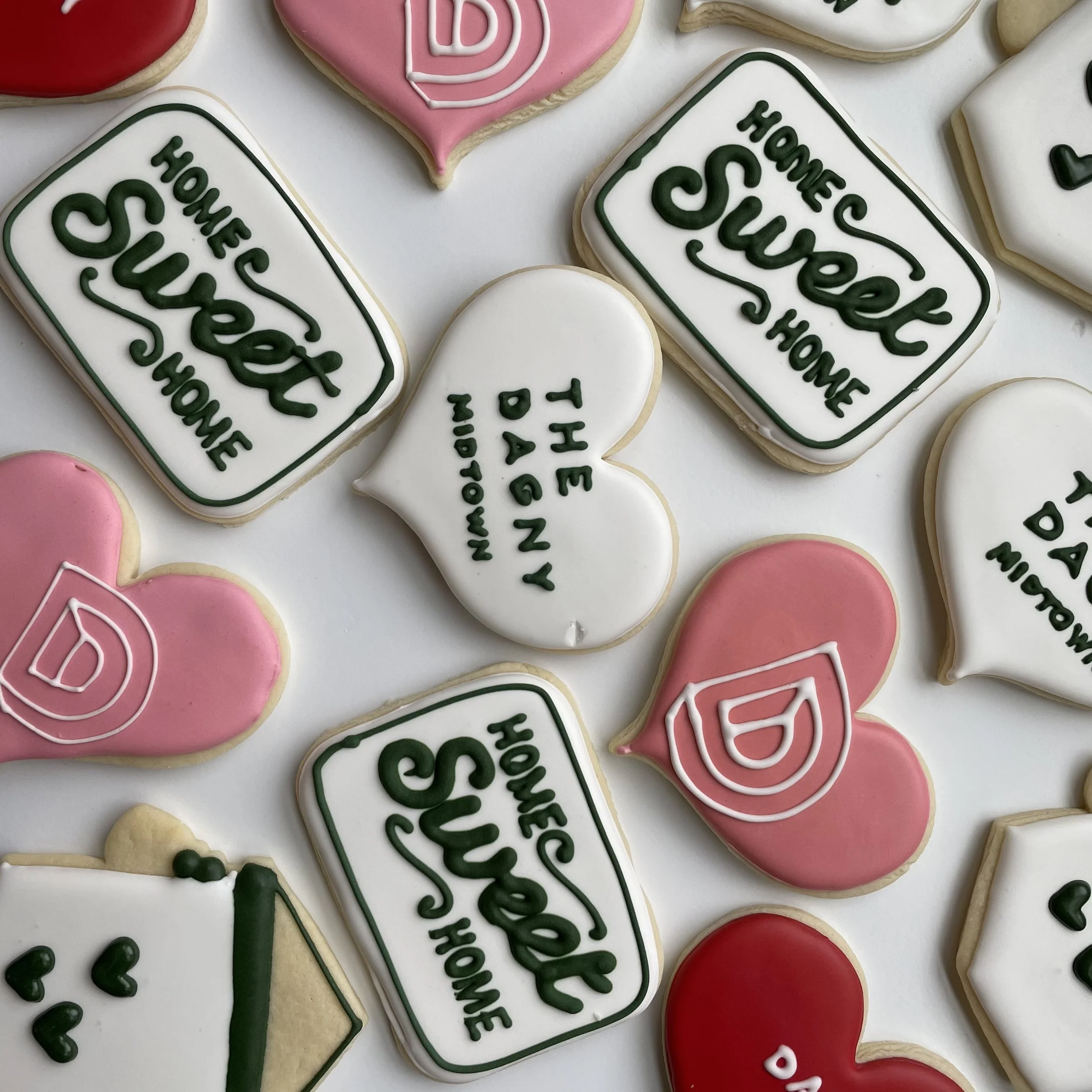 Various decorated cookies with messages like "Home Sweet Home" in green icing, hearts in pink and red icing, and speech bubbles with romantic messages, all on a white background.