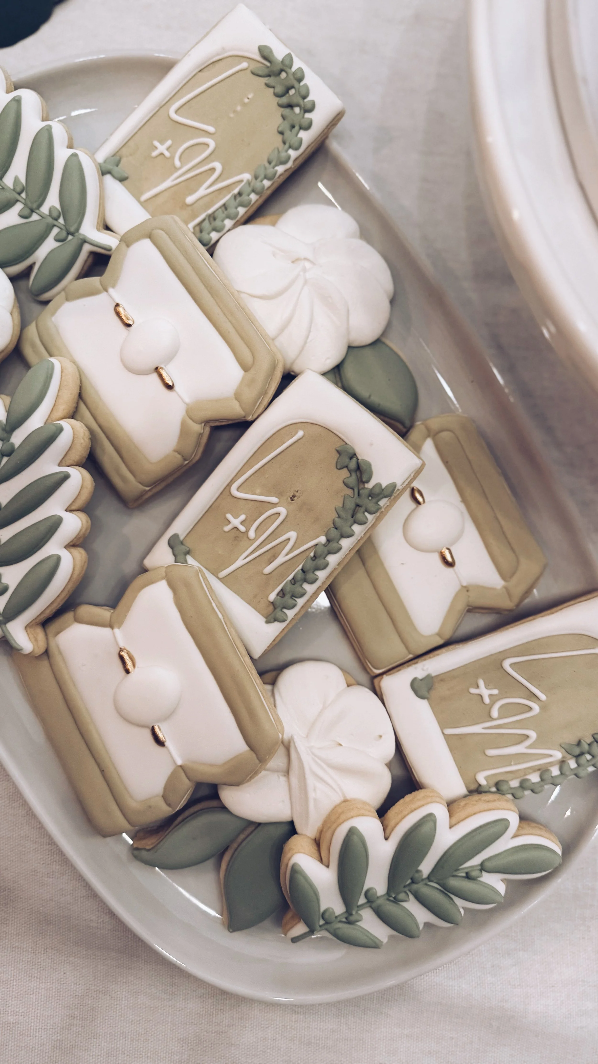 Collection of decorated cookies with a green and white color scheme, featuring leaves, pumpkins, and wedding-themed designs on a white platter.