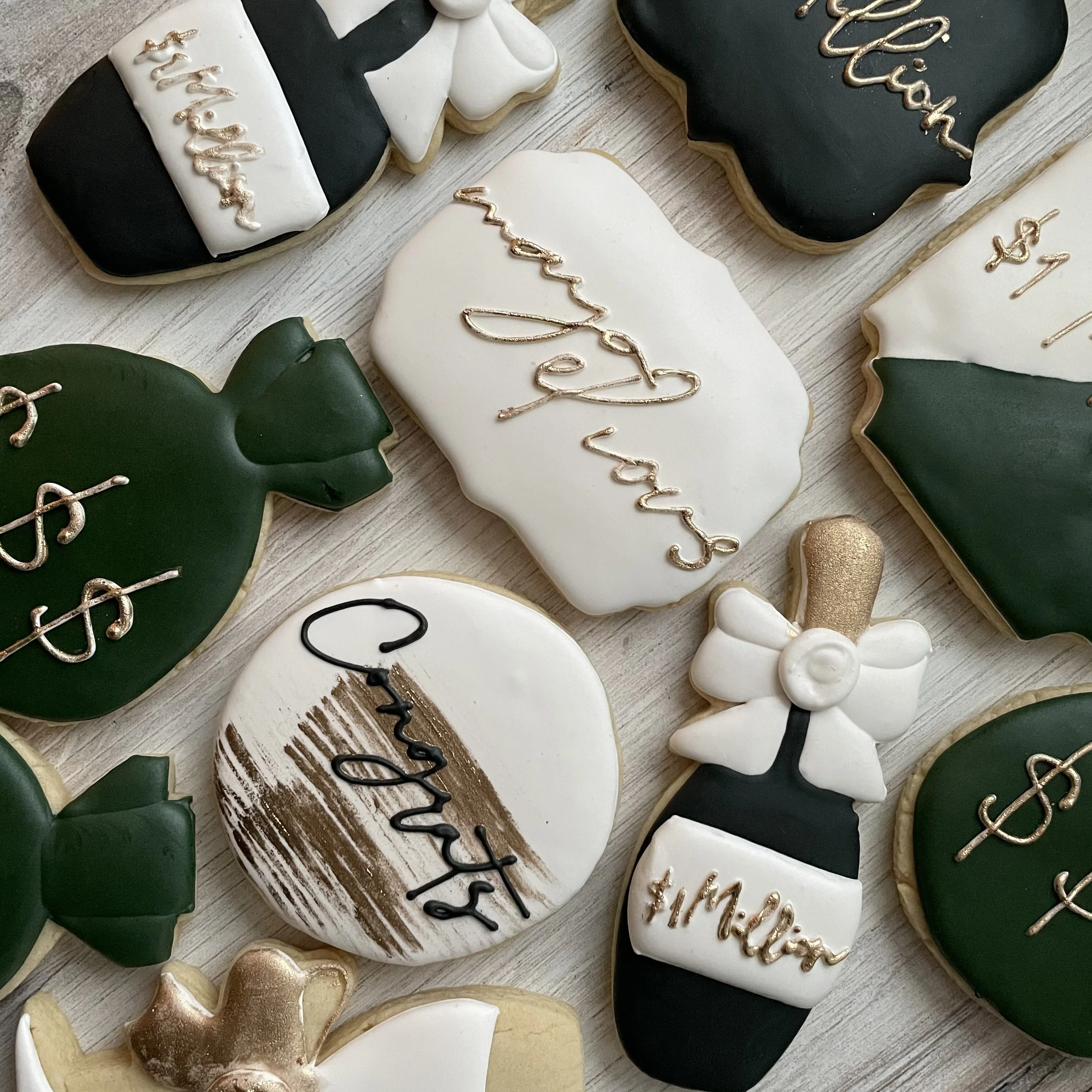 Cookies decorated for Halloween with black, white, and gold icing. Some cookies have the word 'Trick' and 'Treat' written with gold icing, and others have Halloween-themed shapes such as hearts and ghosts. The cookies are arranged on a light wooden s