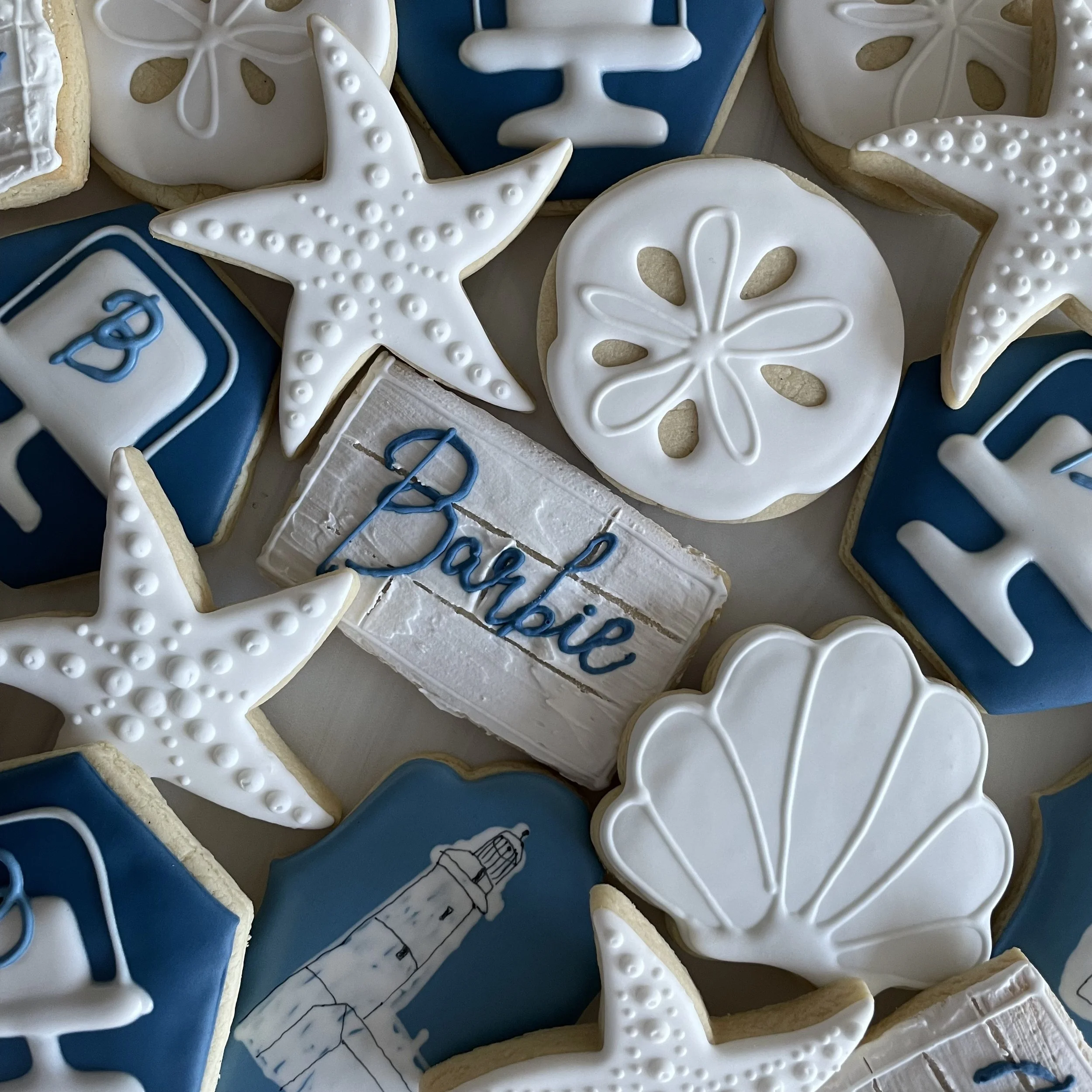 Close-up of decorated cookies with white, blue, and black icing, featuring starfish, peace sign, and a bottle with a cork.