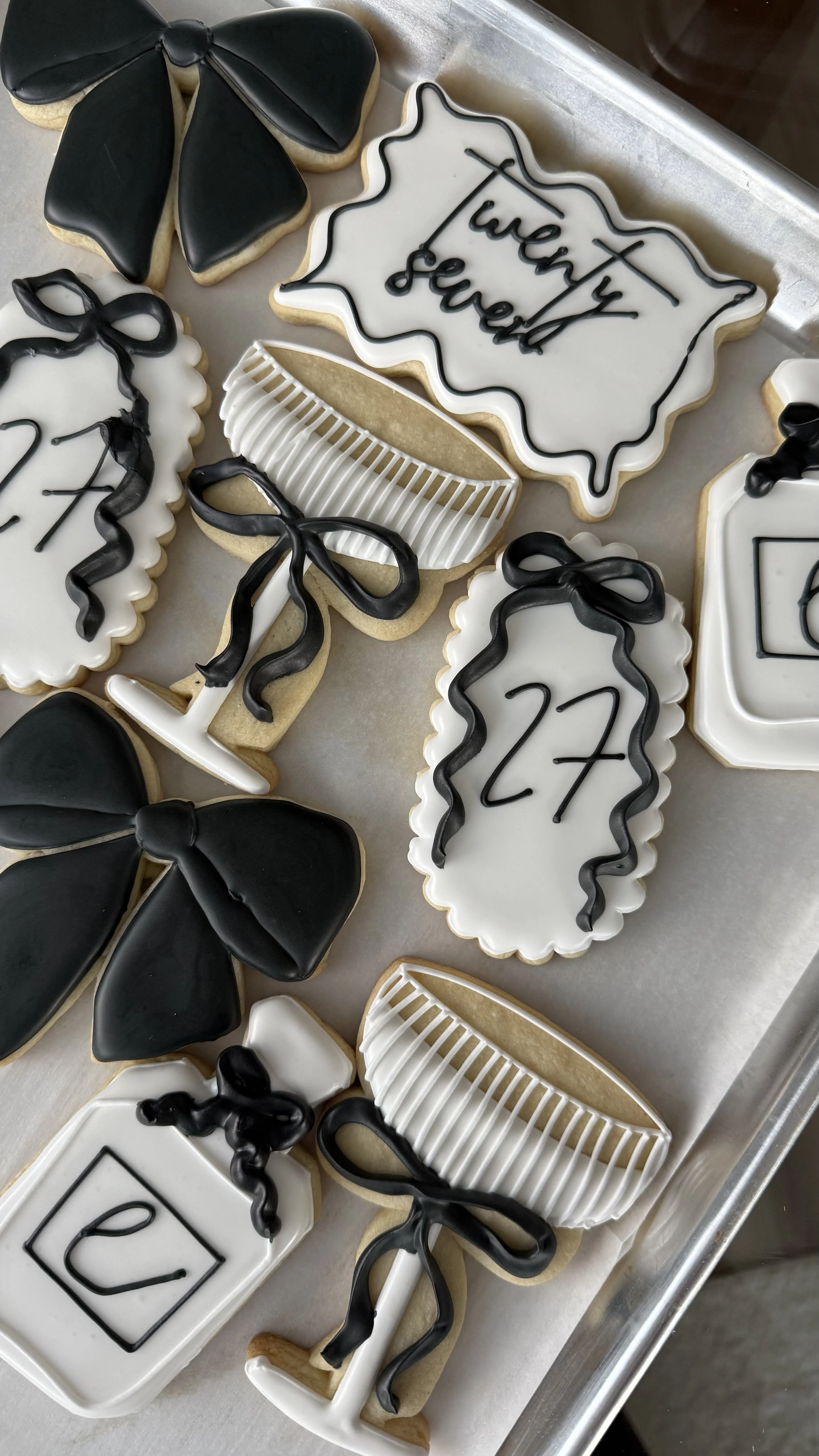 Decorated cookies for a celebration, including a sign reading "Twenty seven years," a champagne bottle, a champagne glass, and a bow, all in black and white color themes.
