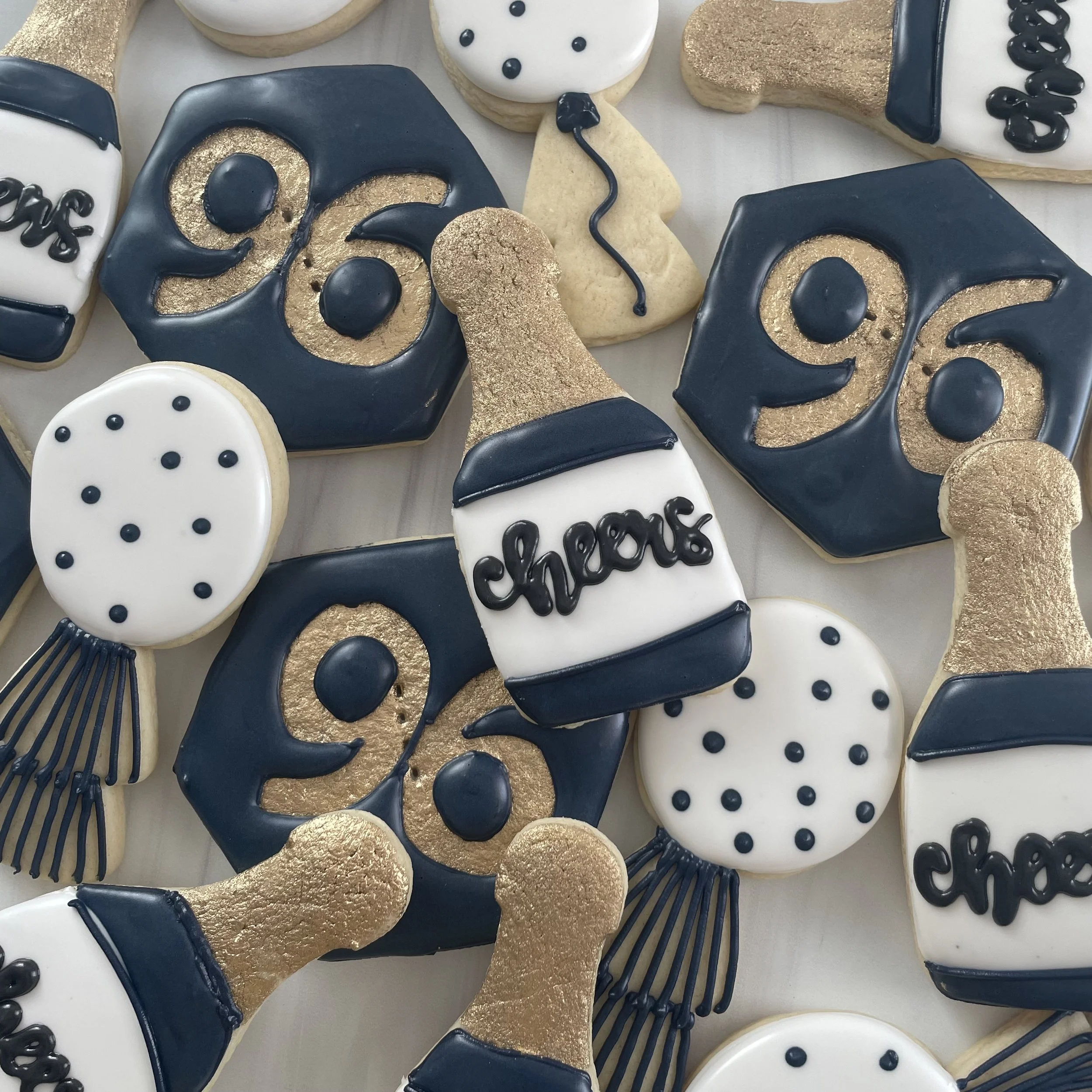 Decorative cookies with various designs in black, white, and gold icing, including skulls, butterflies, with some featuring gold leaf accents.