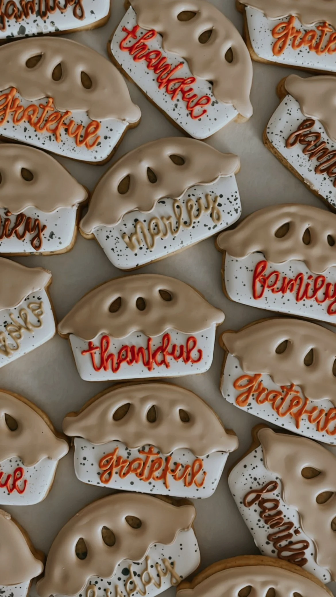 Decorated cookies shaped like pumpkins with messages such as "thankful," "grateful," and "happy" written on them in orange and beige icing.