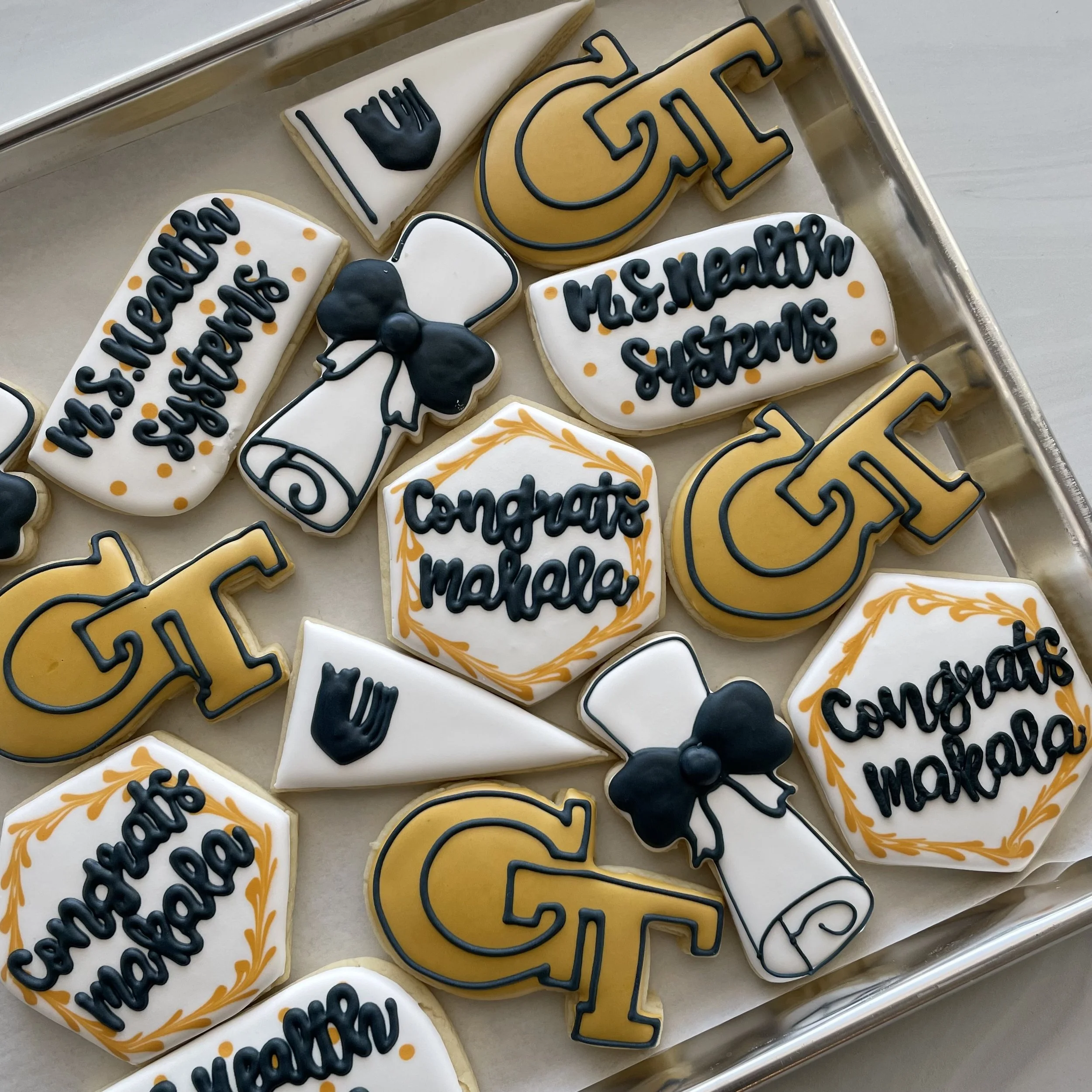 Cookies decorated with black and orange icing, featuring various shapes and words like "Happy Graduation" and "Ms. Hart" in black icing.