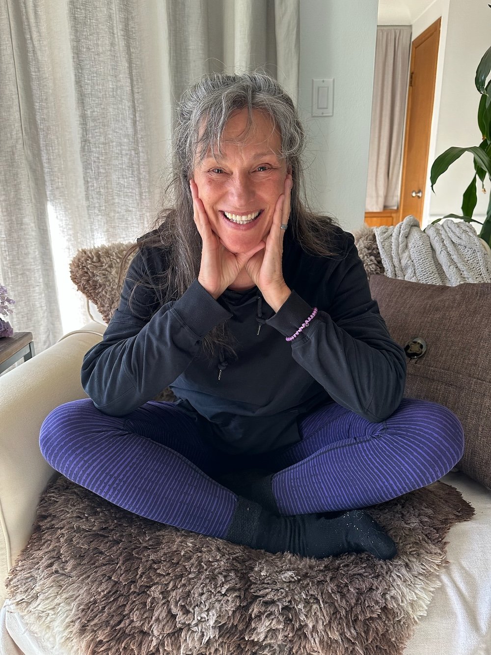 Rita Henry cross legged on a chair smiling at the camera