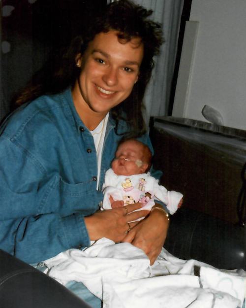 Rita Henry holding a newborn baby, Julia, with a nasal oxygen tube, in a hospital or medical setting.