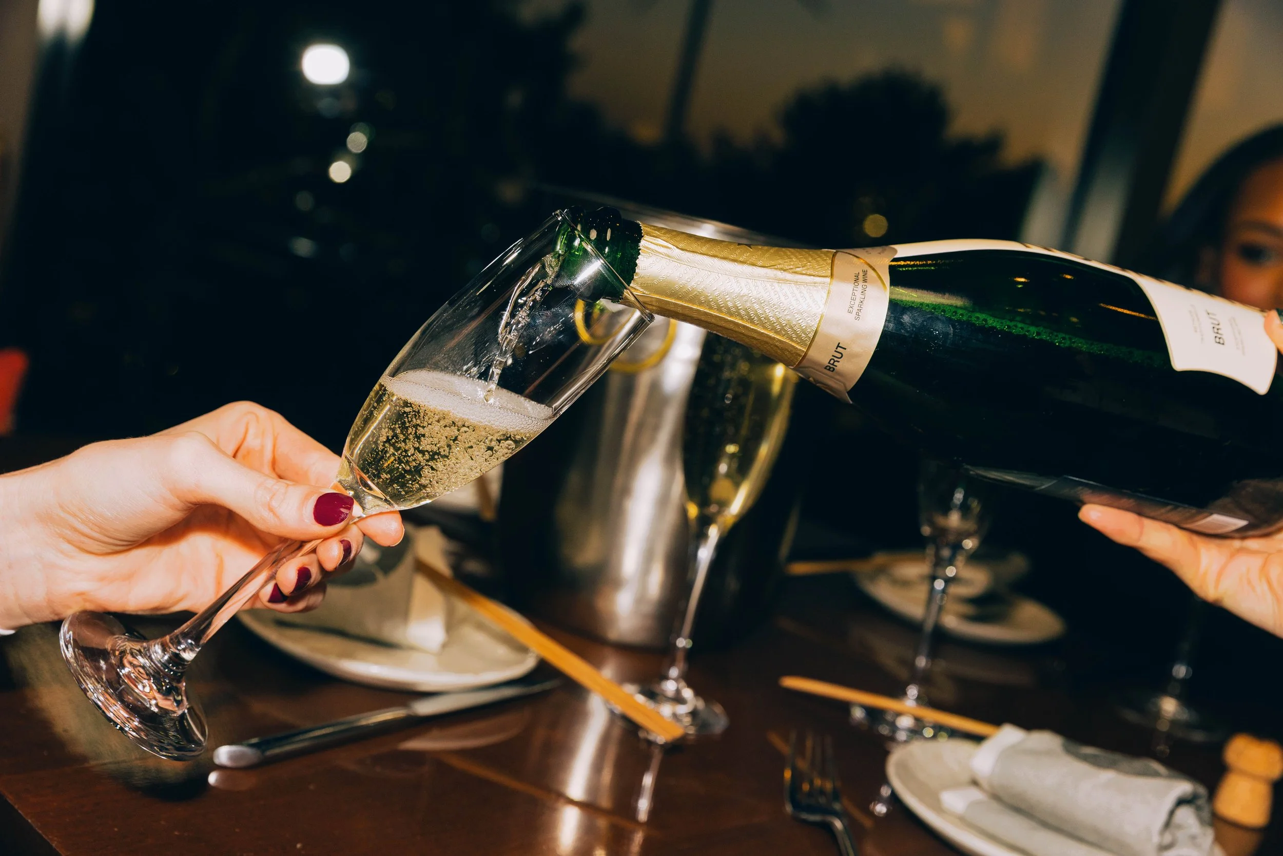 Person pouring champagne from a green bottle into a flute glass at a celebration or Gathering. food and beverage photography.