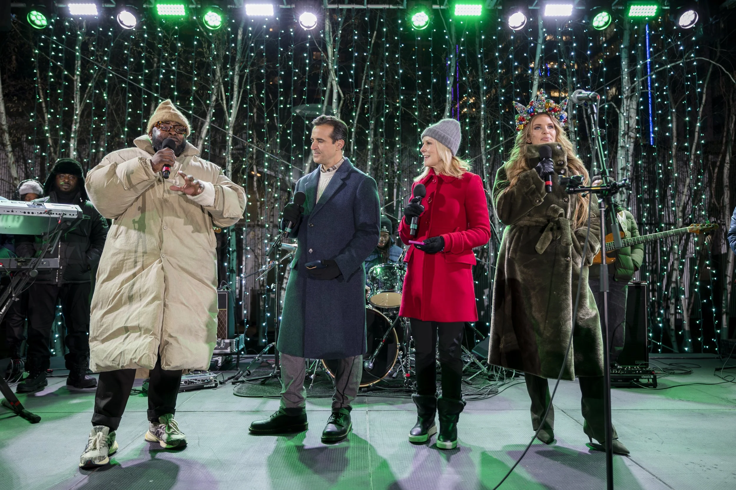 Four people standing on a stage with musical instruments, performing at night with Christmas lights in the background. Seaport event photography. 