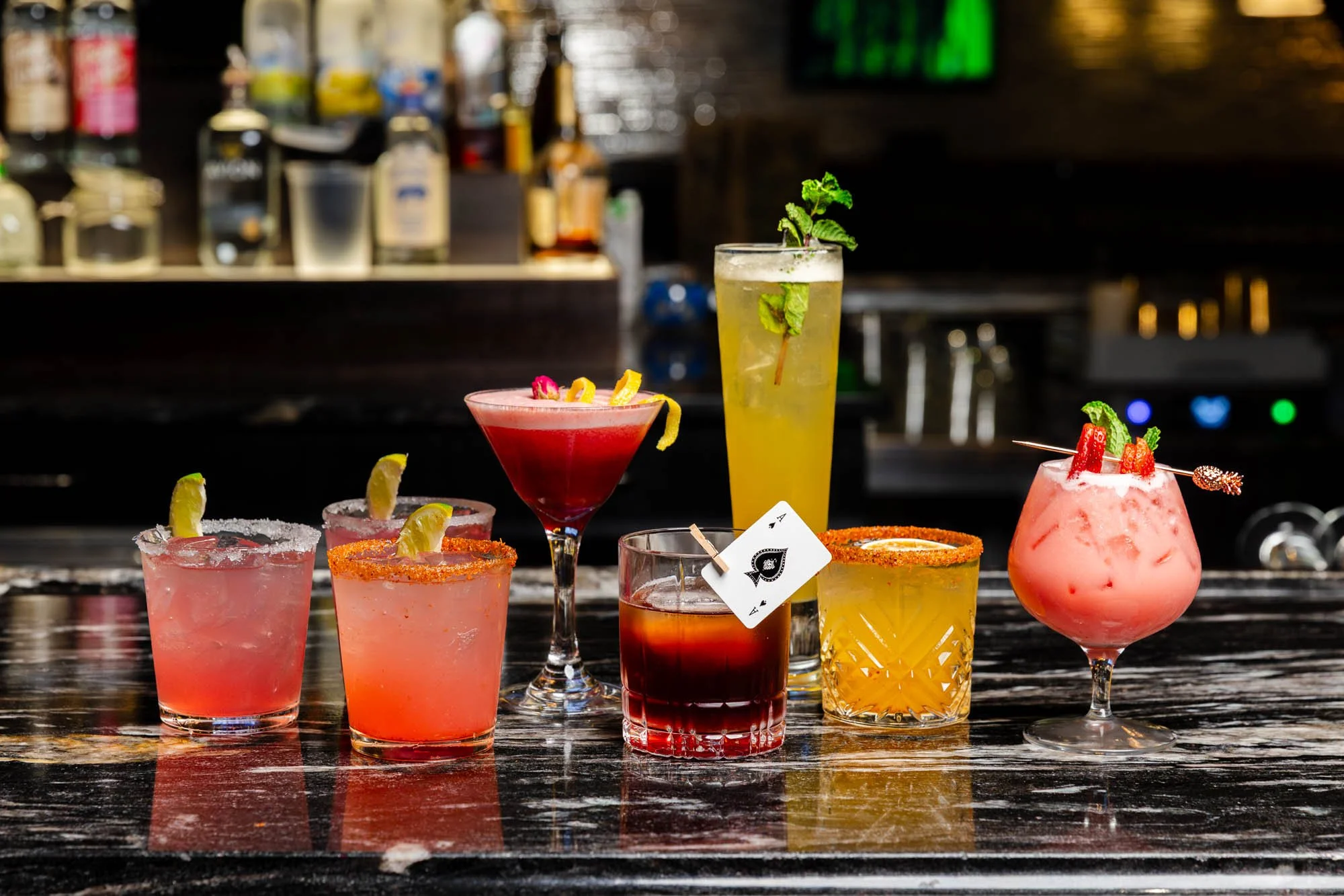 Various colorful cocktails on a bar counter, with a blurred background of liquor bottles and bar equipment. food and beverage photography.
