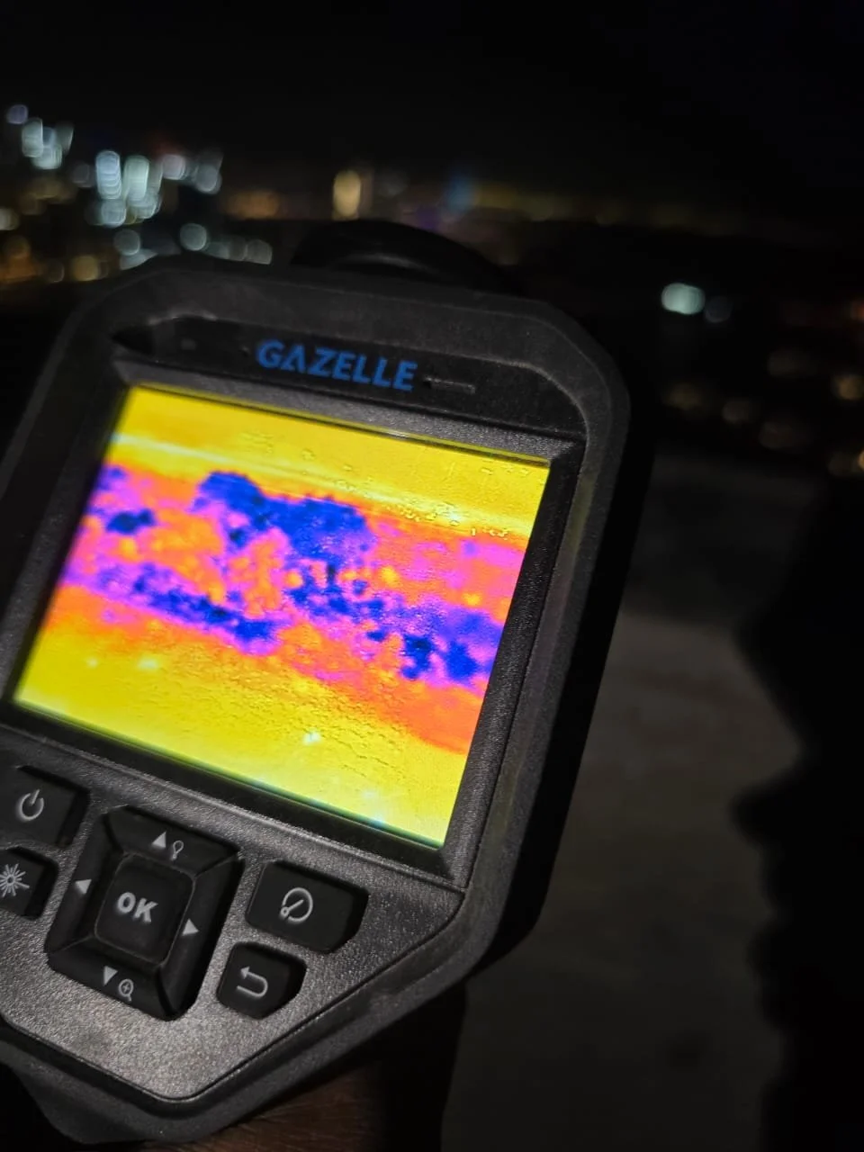 A thermal imaging device displays a colorful thermal image with blue, purple, orange, and yellow areas.