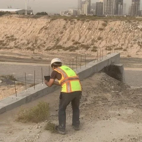 Construction worker in a safety vest and helmet taking notes or measurements on a concrete barrier at a construction site.