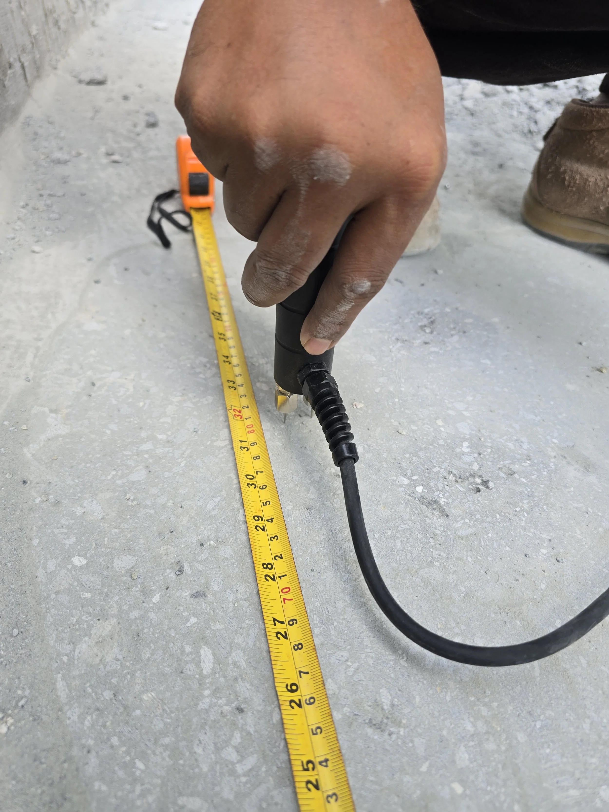 A person working with a measuring tape and using a moisture meter to perform a Moisture Test on a concrete floor.