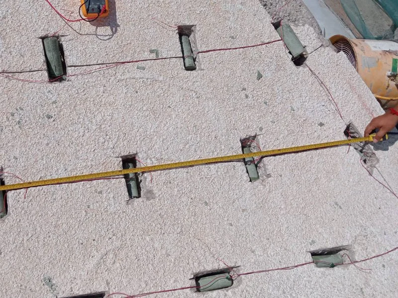 A worker measures spacing between anodes embedded in concrete.
