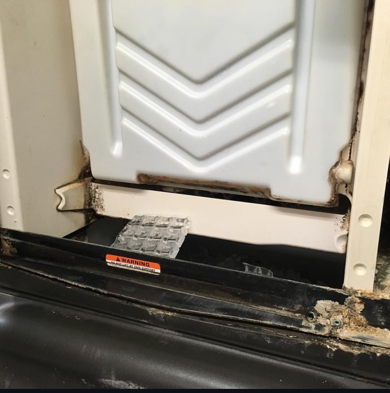 Close-up of a dirty, rusty electrical panel or appliance with visible corrosion and a warning sticker at the bottom.