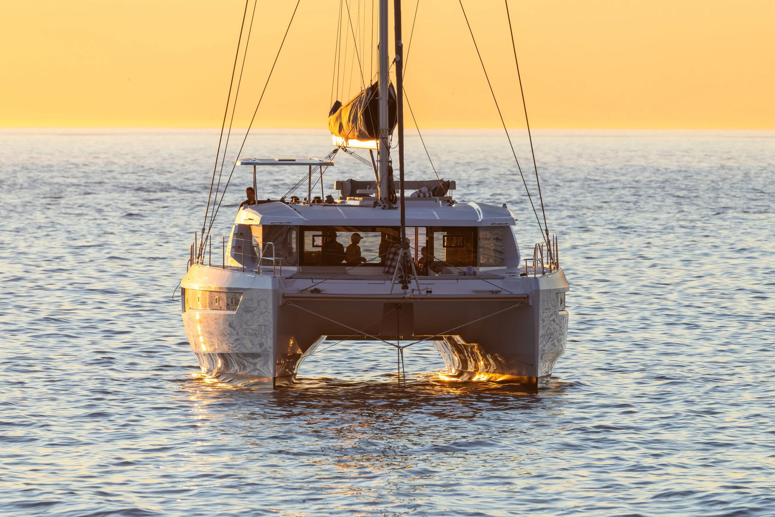 A catamaran sailboat on the water at sunset with a person on board.