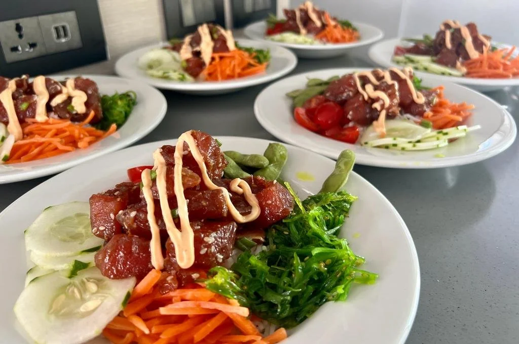 Several white plates with assorted beef sashimi, shredded carrots, cucumber slices, cherry tomatoes, seaweed, and a drizzle of light-colored dressing, arranged on a gray counter.