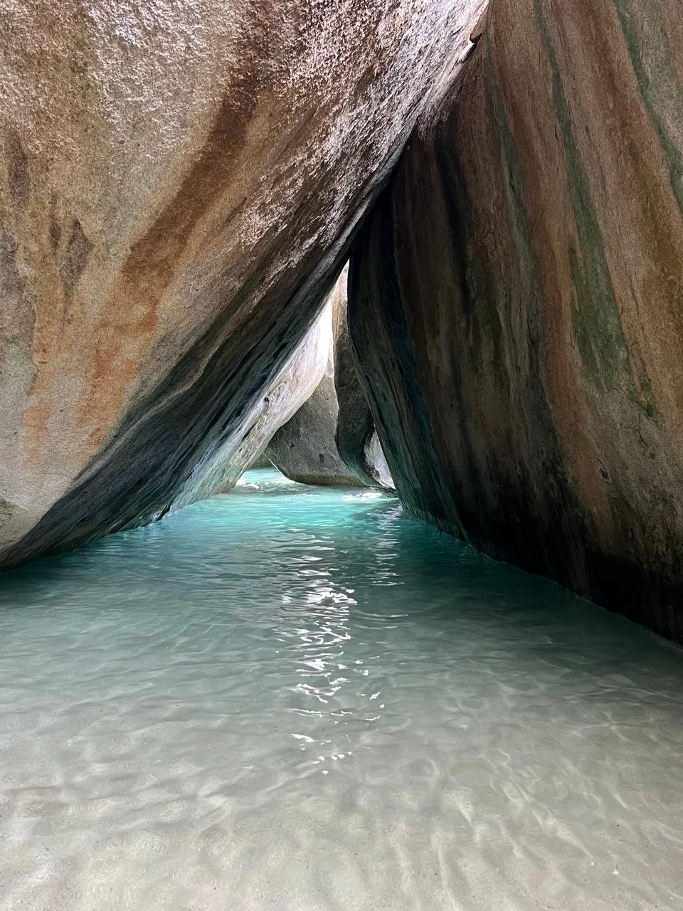A secluded waterway with large, smooth rock formations surrounding clear turquoise water.