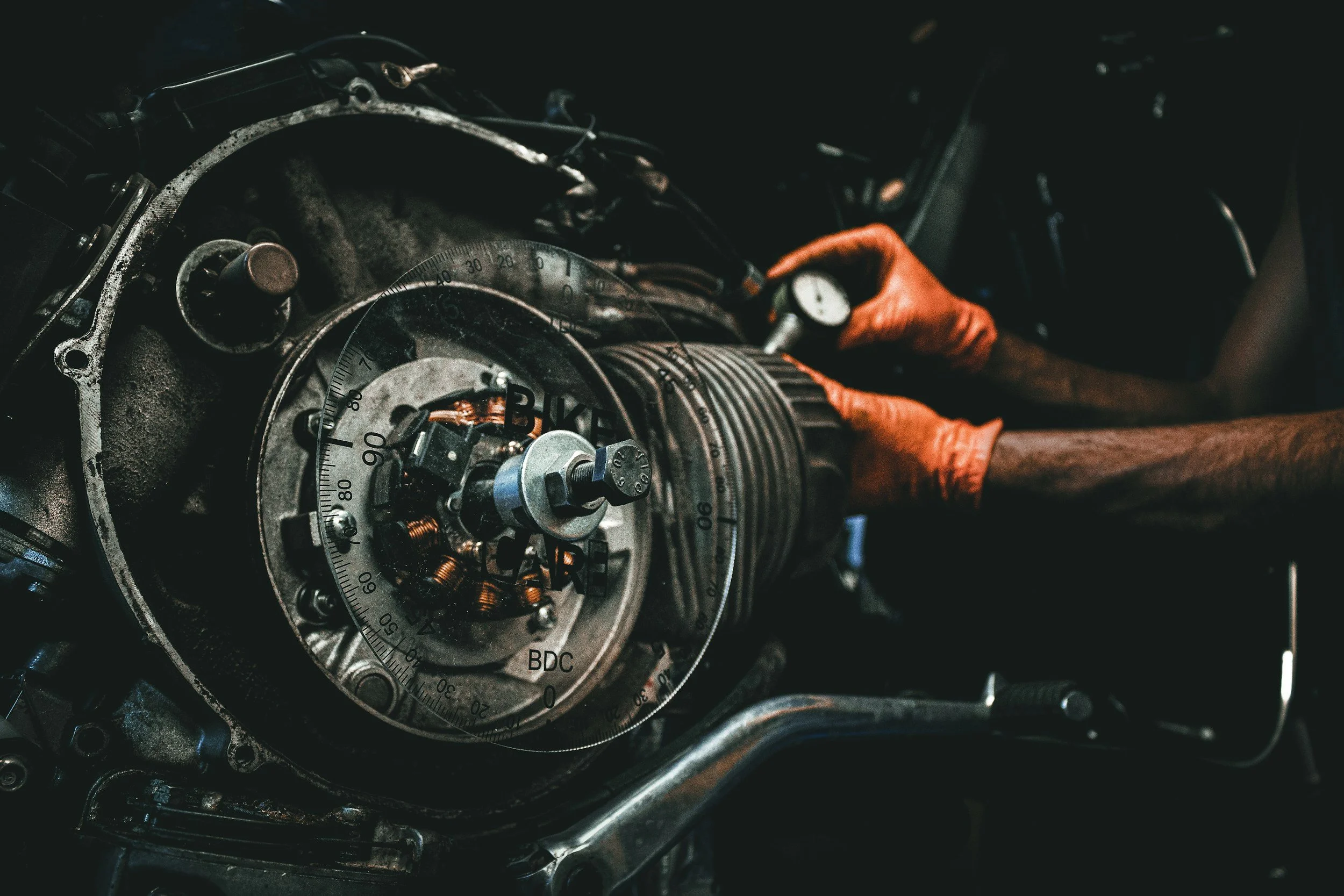 Close-up of a mechanic's hand in an orange glove working on a disassembled motorcycle engine.