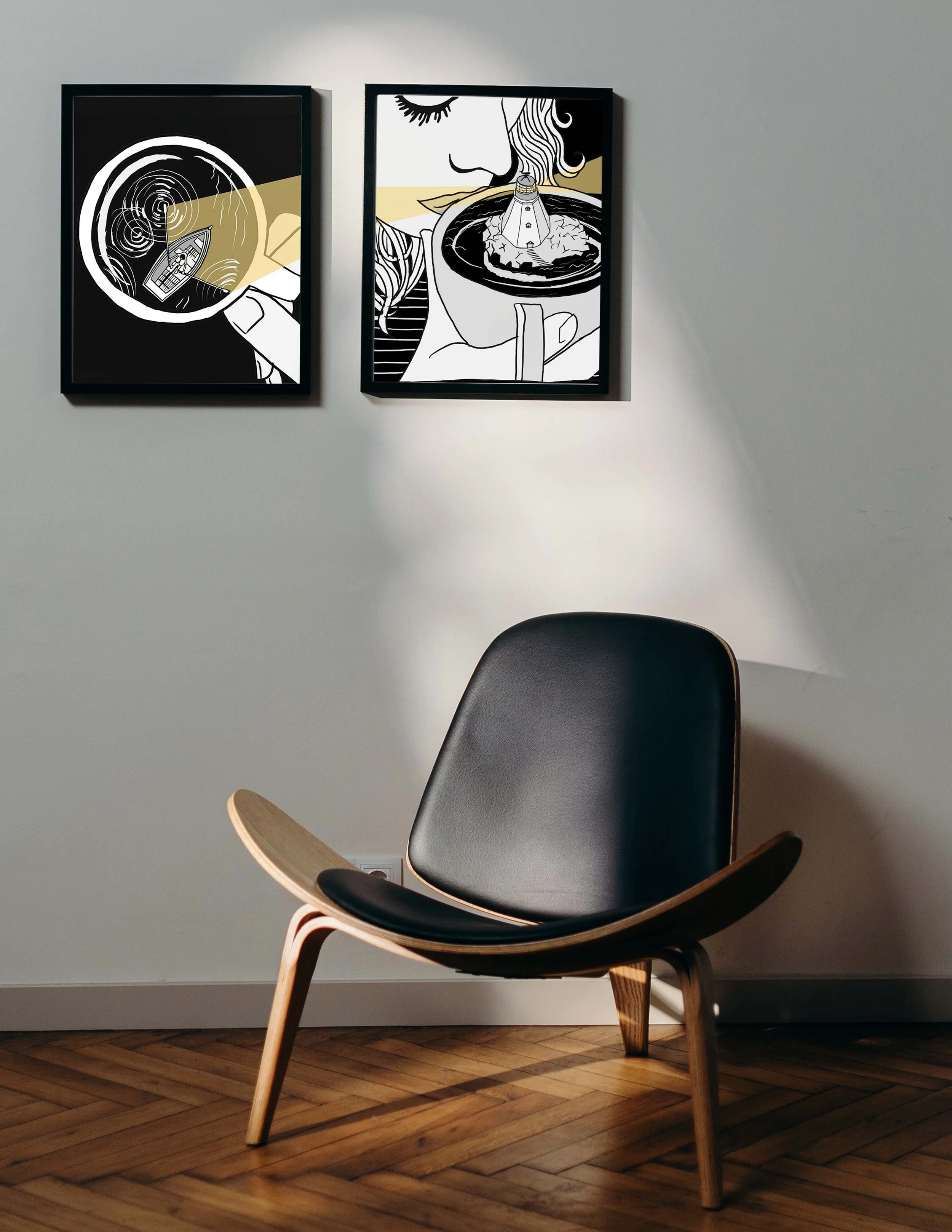 Black armchair in a minimal interior with two framed graphic illustrations above, showing black, white, and gold compositions with light as a central element.