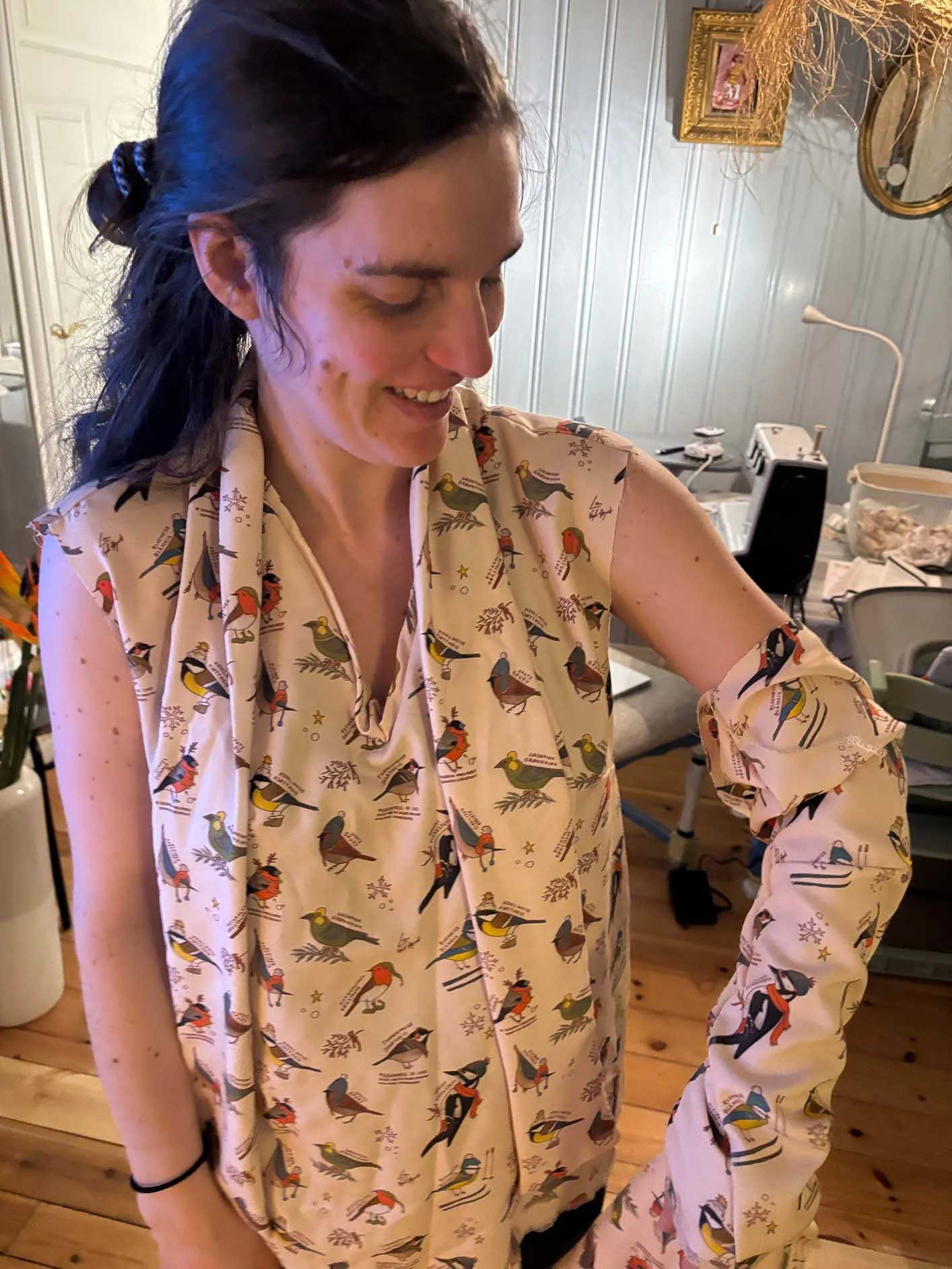 Photo of a woman wearing a partly finished blouse made from fabric with a winter bird pattern, showing the illustration translated into textile form.