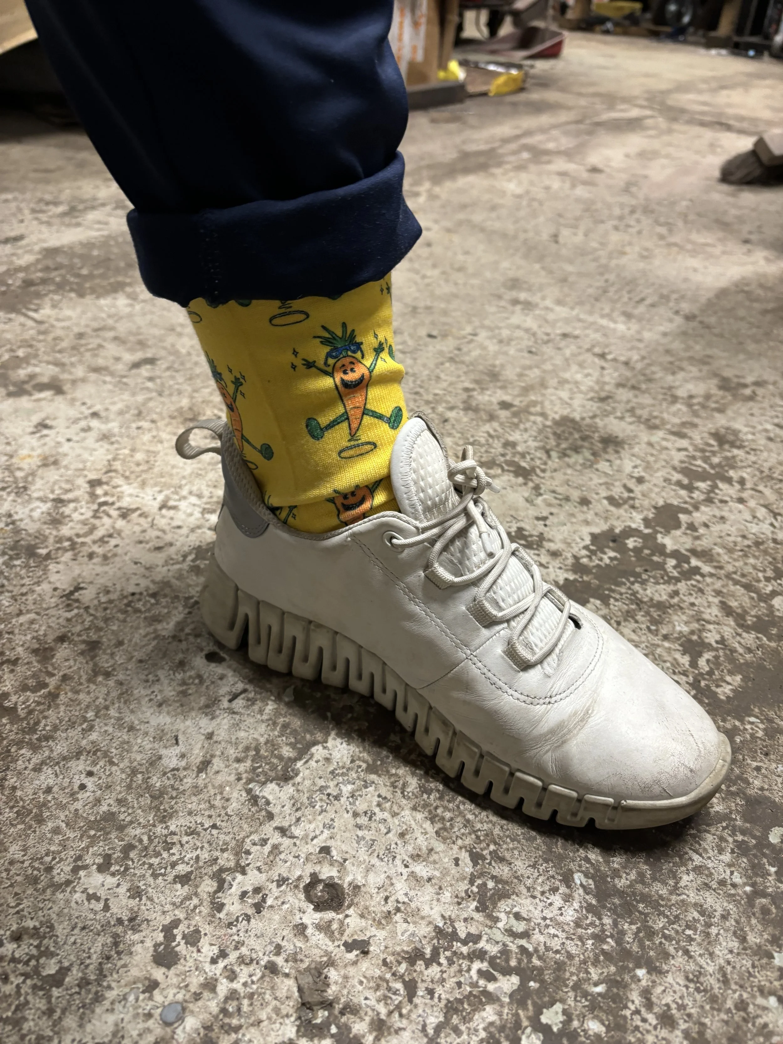 Close-up of a white sneaker worn with a bright yellow sock featuring a repeating pattern of illustrated carrots.
