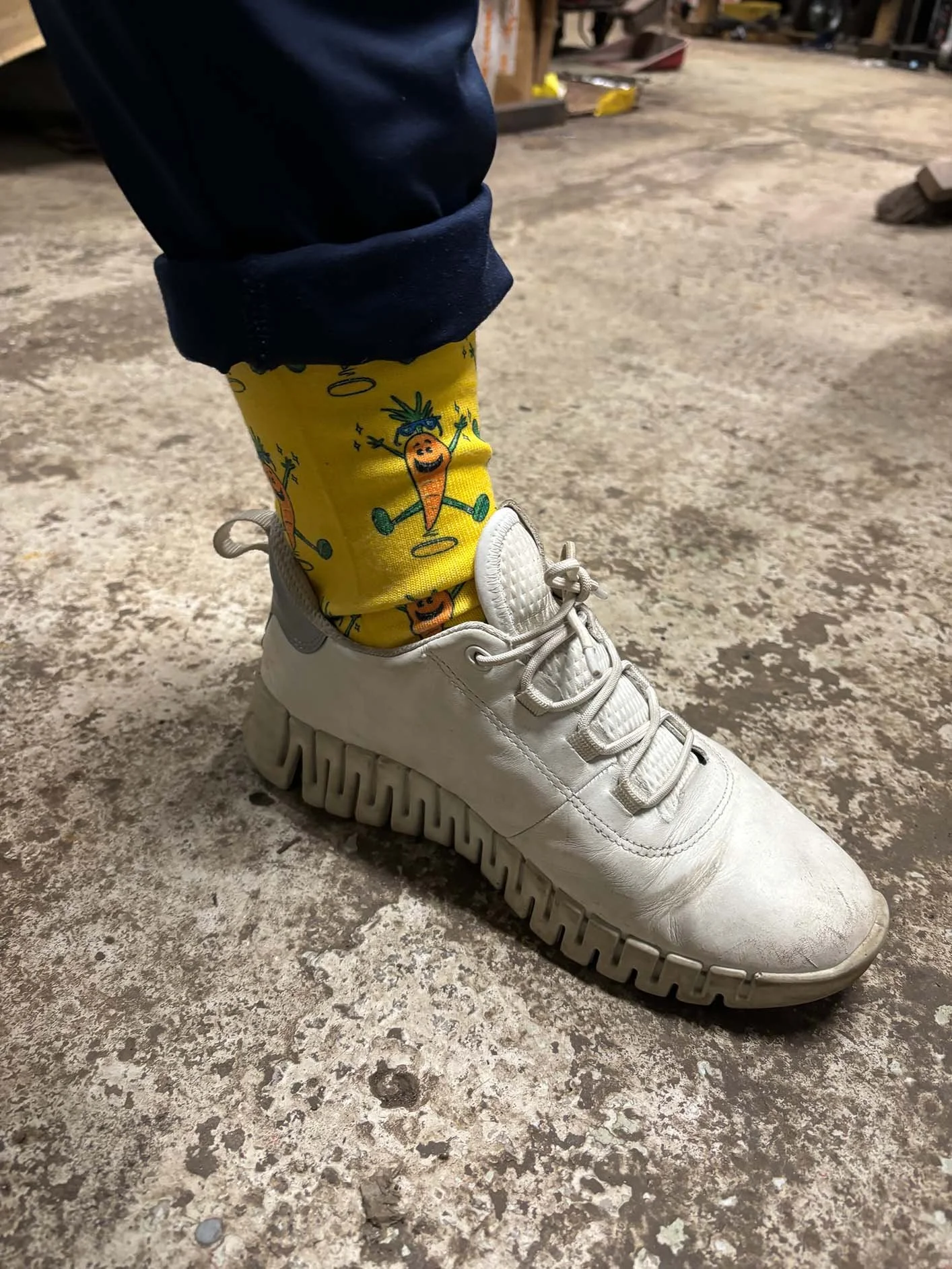 Close-up of a white sneaker worn with a bright yellow sock featuring a repeating pattern of illustrated carrots.