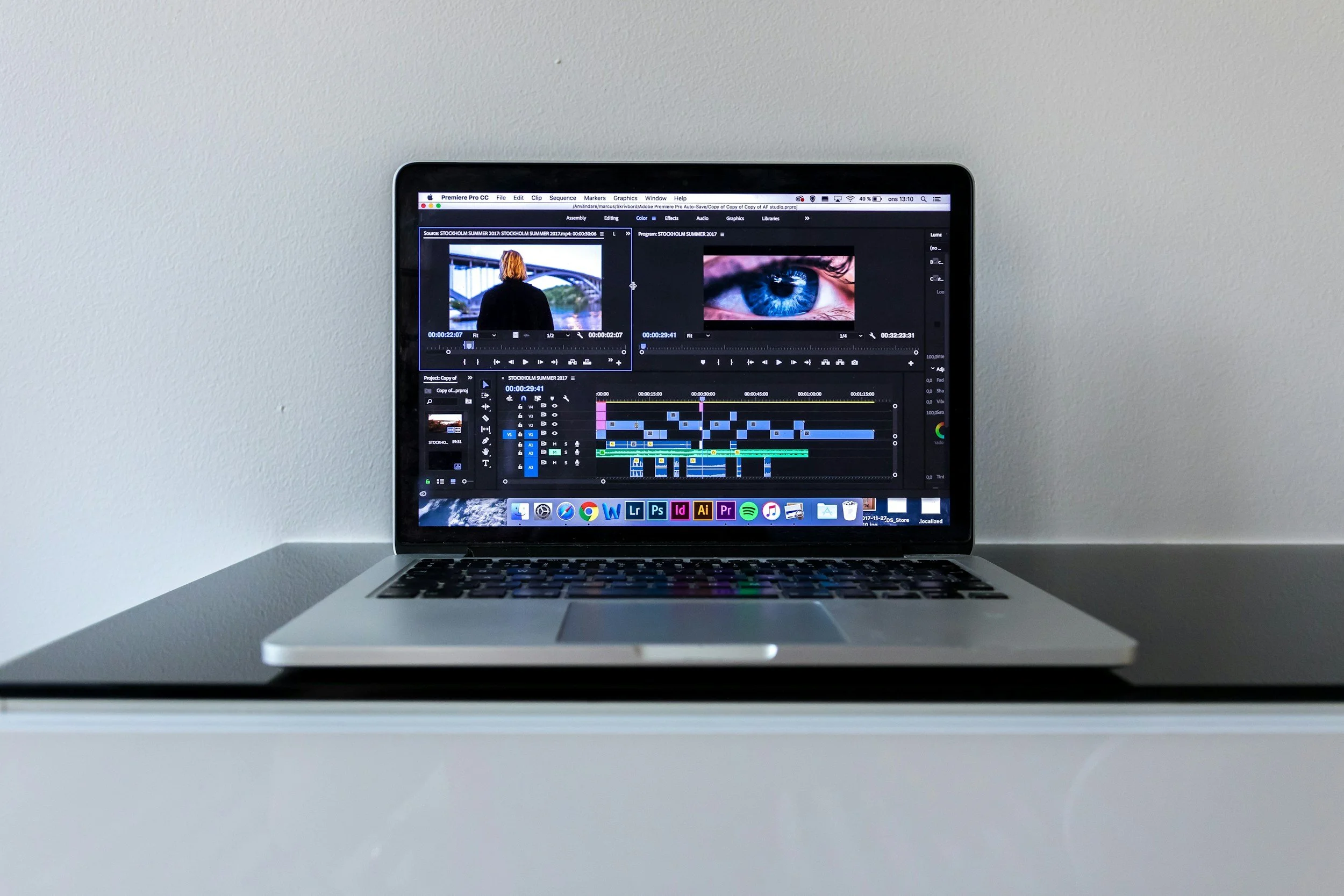Open laptop on a white desk, displaying video editing software with clips, timelines, and images of a woman and a close-up of a blue eye.