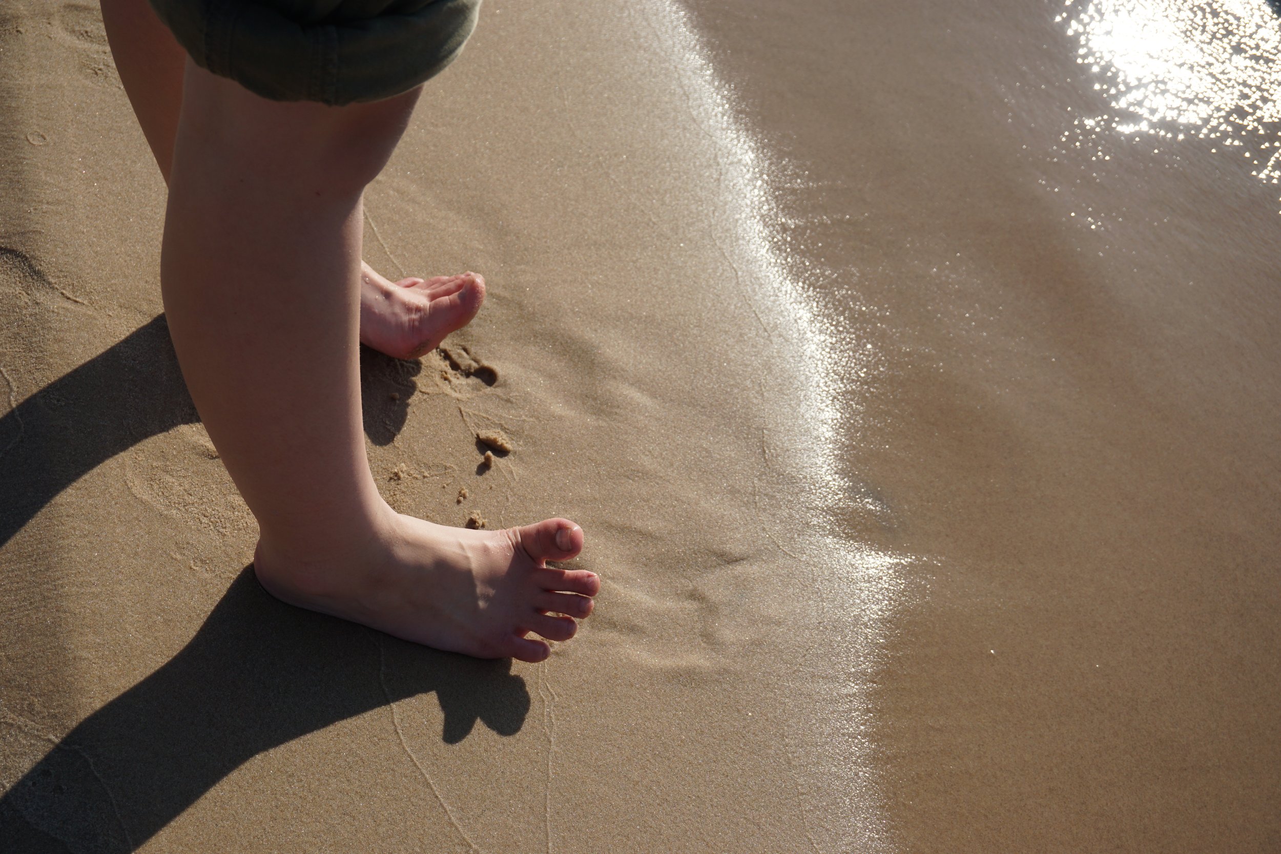 Child's legs and feet in the sand near the water at the beach.