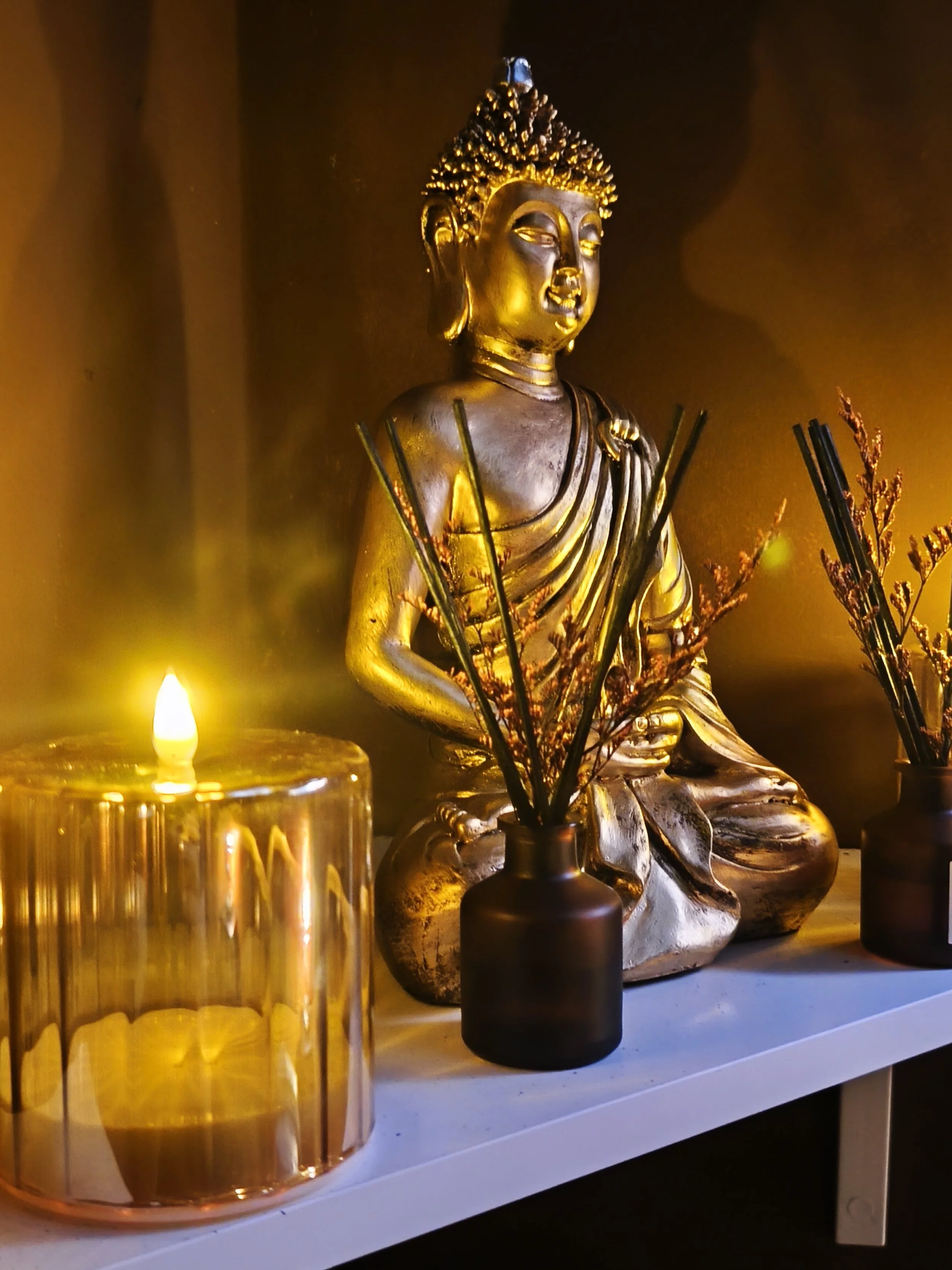 Estatua de Buda dorada con velas y plantas decorativas en un altar.