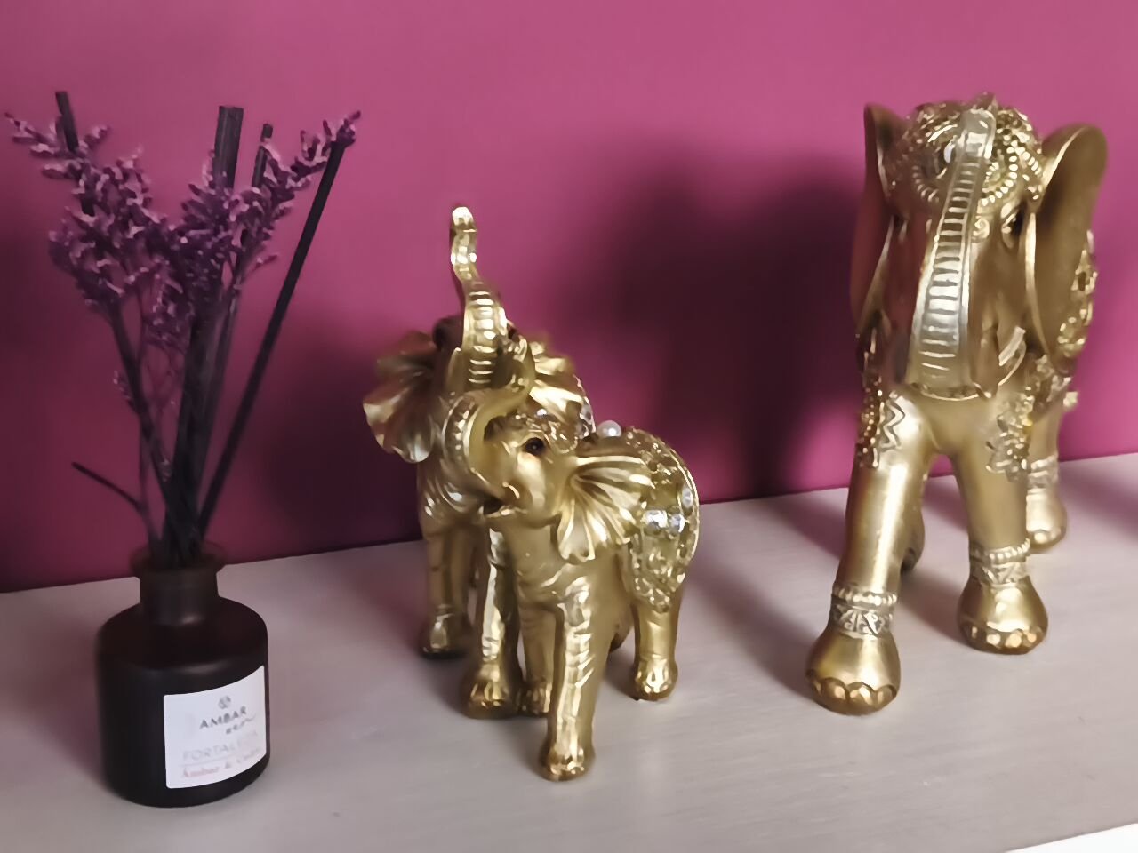 Decoración con figuras de elefantes dorados, una flor seca en un jarrón negro y fondo rosa.