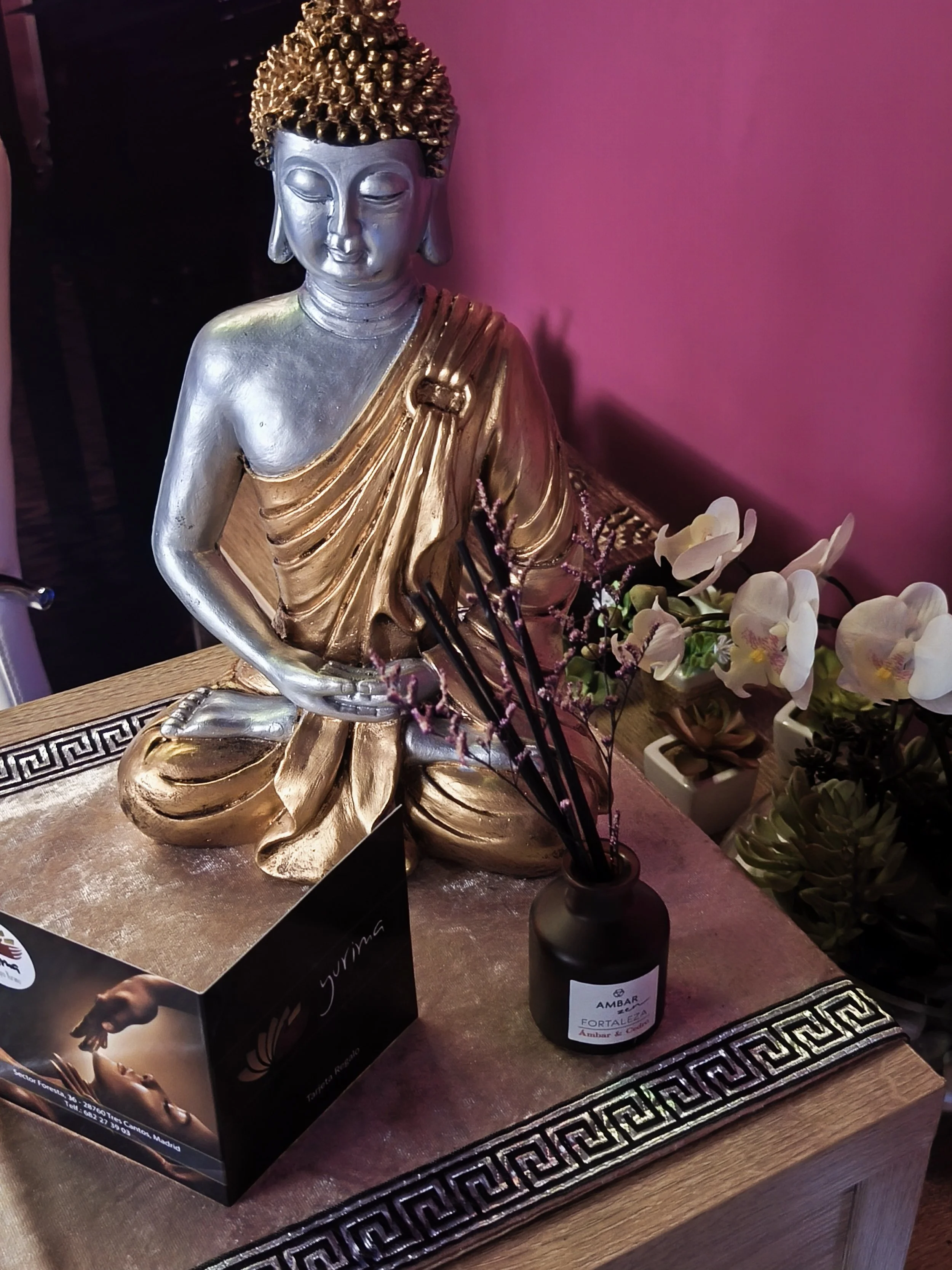 Estatua de Buda dorada en un lugar decorado con flores blancas y un fondo rosado.