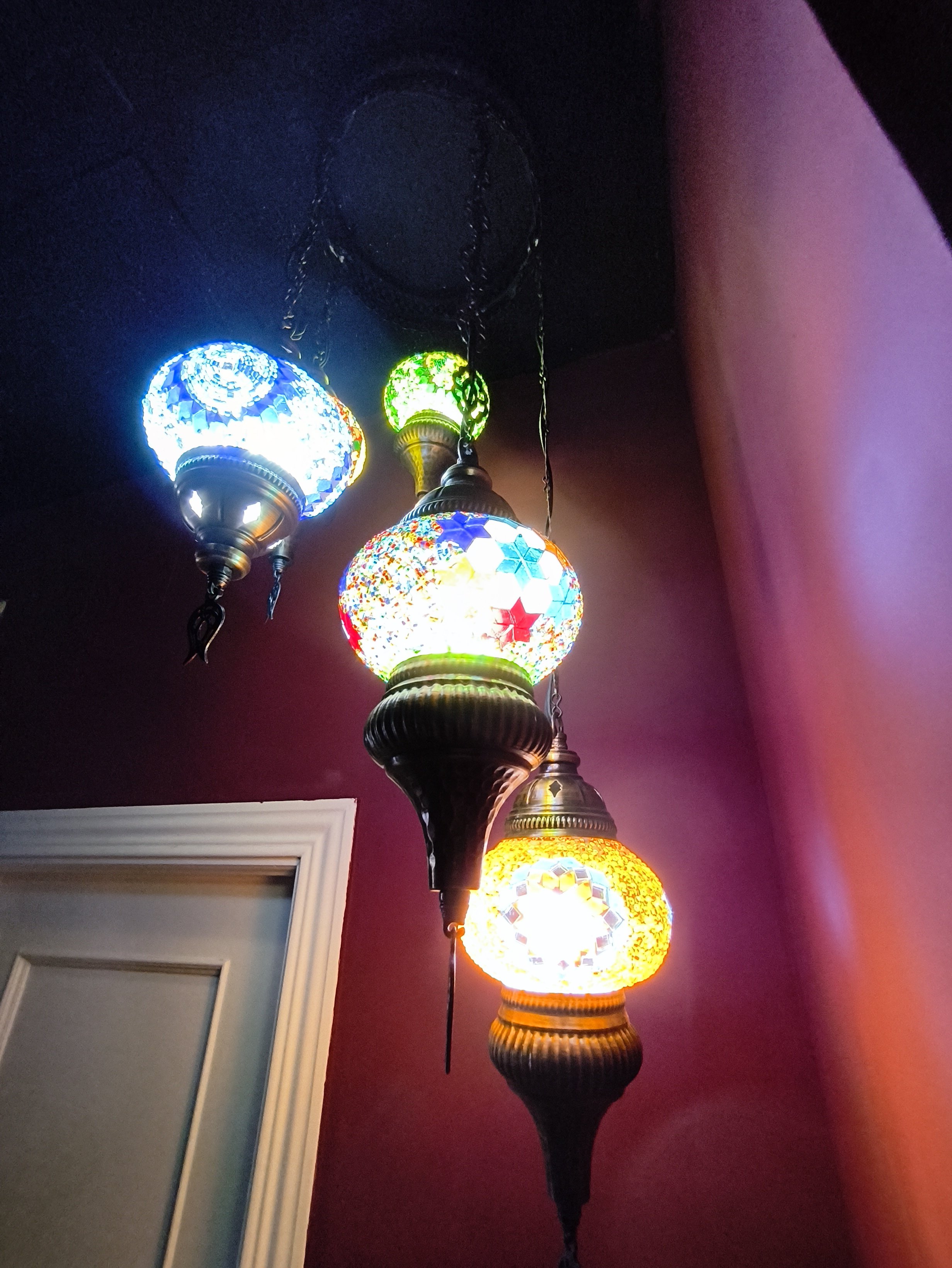 Un candelabro con varias pantallas de lámparas de colores vivos, en un fondo oscuro y una pared de color vino.