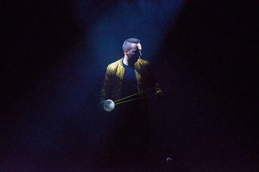 Un homme portant une veste dorée se tient dans l'obscurité, tenu un objet avec des câbles lumineux.