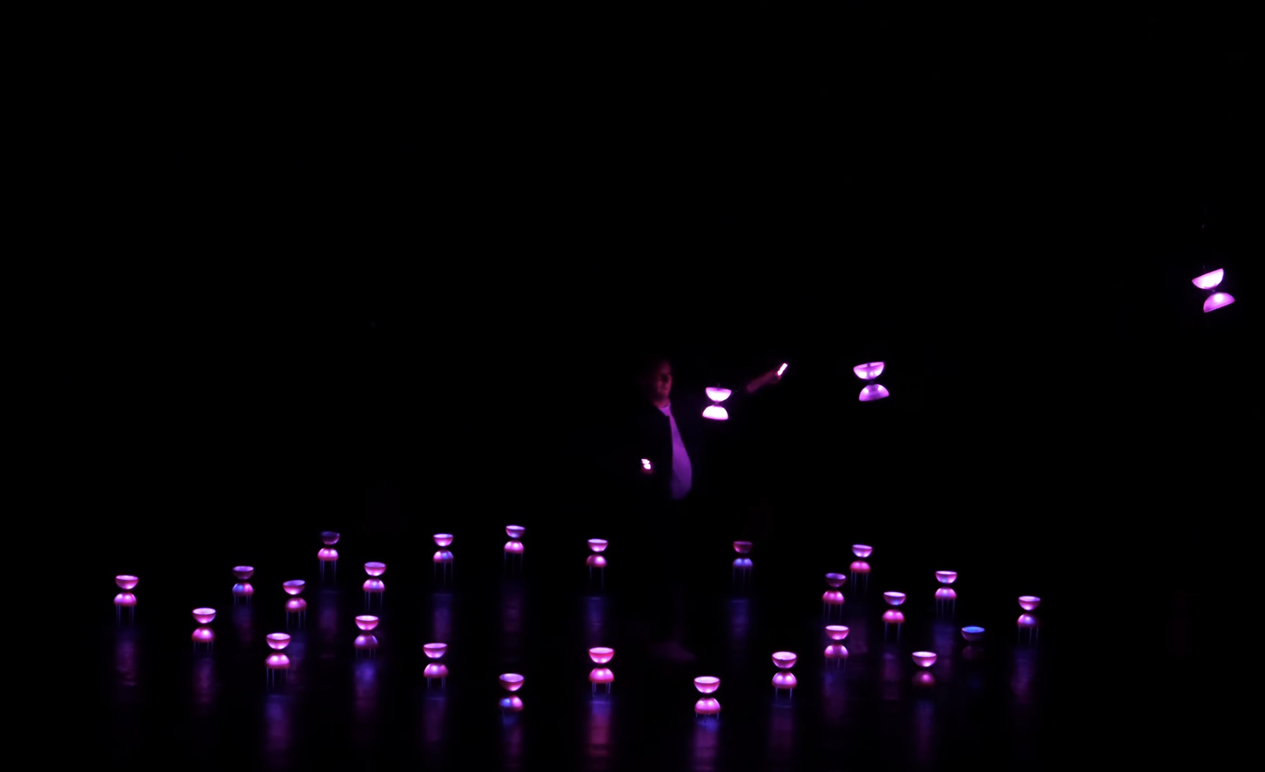 Une personne dans l'obscurité manipulant des lampes de couleur violette, avec des effets lumineux créant une ambiance mystérieuse.