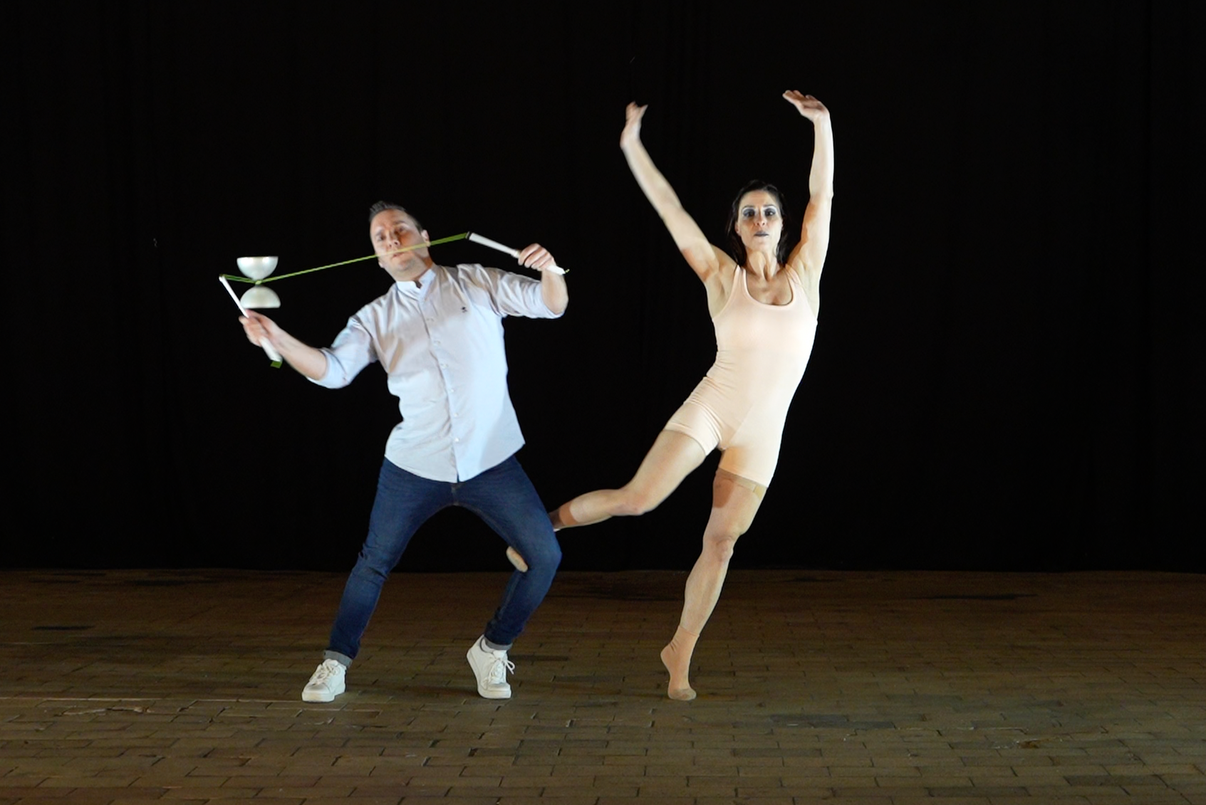 Deux artistes effectuant une performance de danse contemporaine sur scène avec un fond noir, l'un joue avec un diabolo et l'autre pose dans une posture artistique