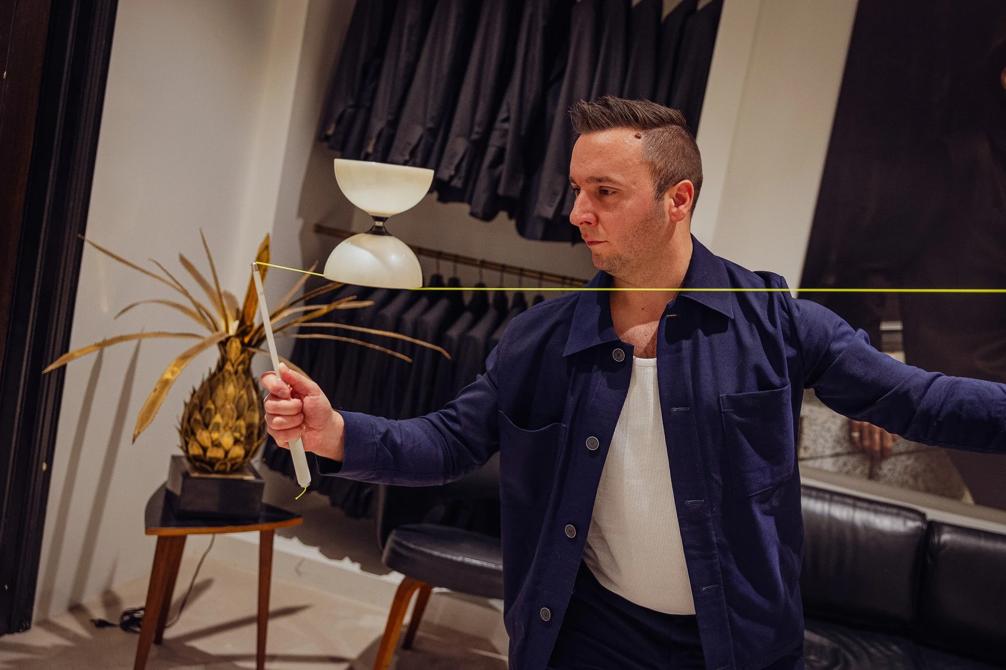 Un homme regarde dans un miroir tout en tenant une baguette ou un bâton blanc, dans un environnement intérieur moderne avec un vase décoratif en forme d'ananas sur une table à côté.