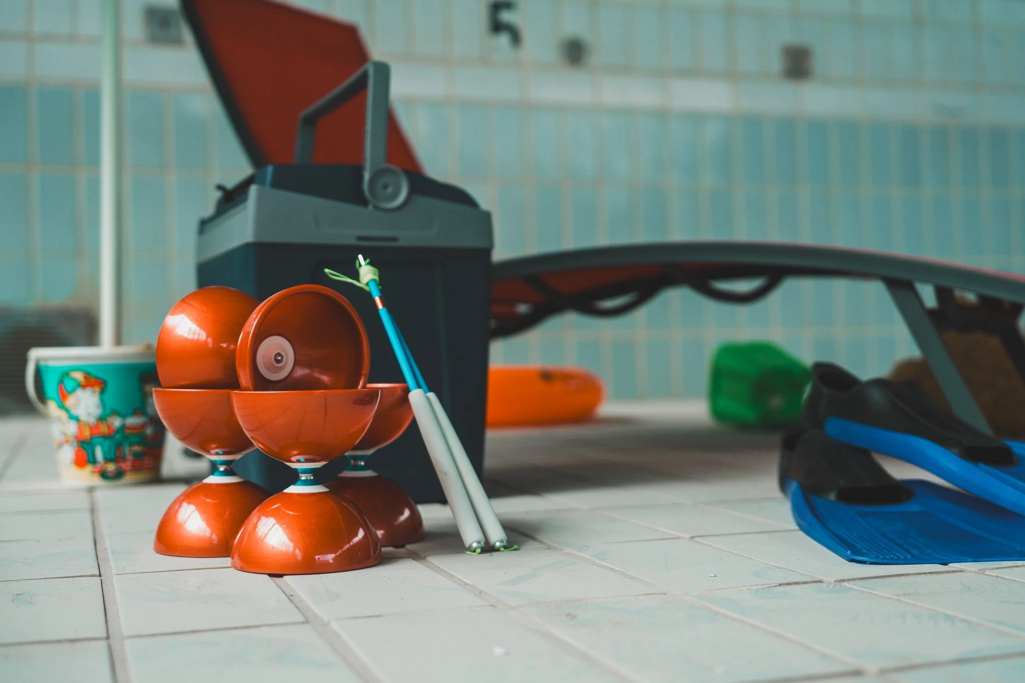 Des jouets d'enfants sur le sol, y compris des ballons orange, un seau, un arrosoir vert et un skate bleu, avec un environnement intérieur.