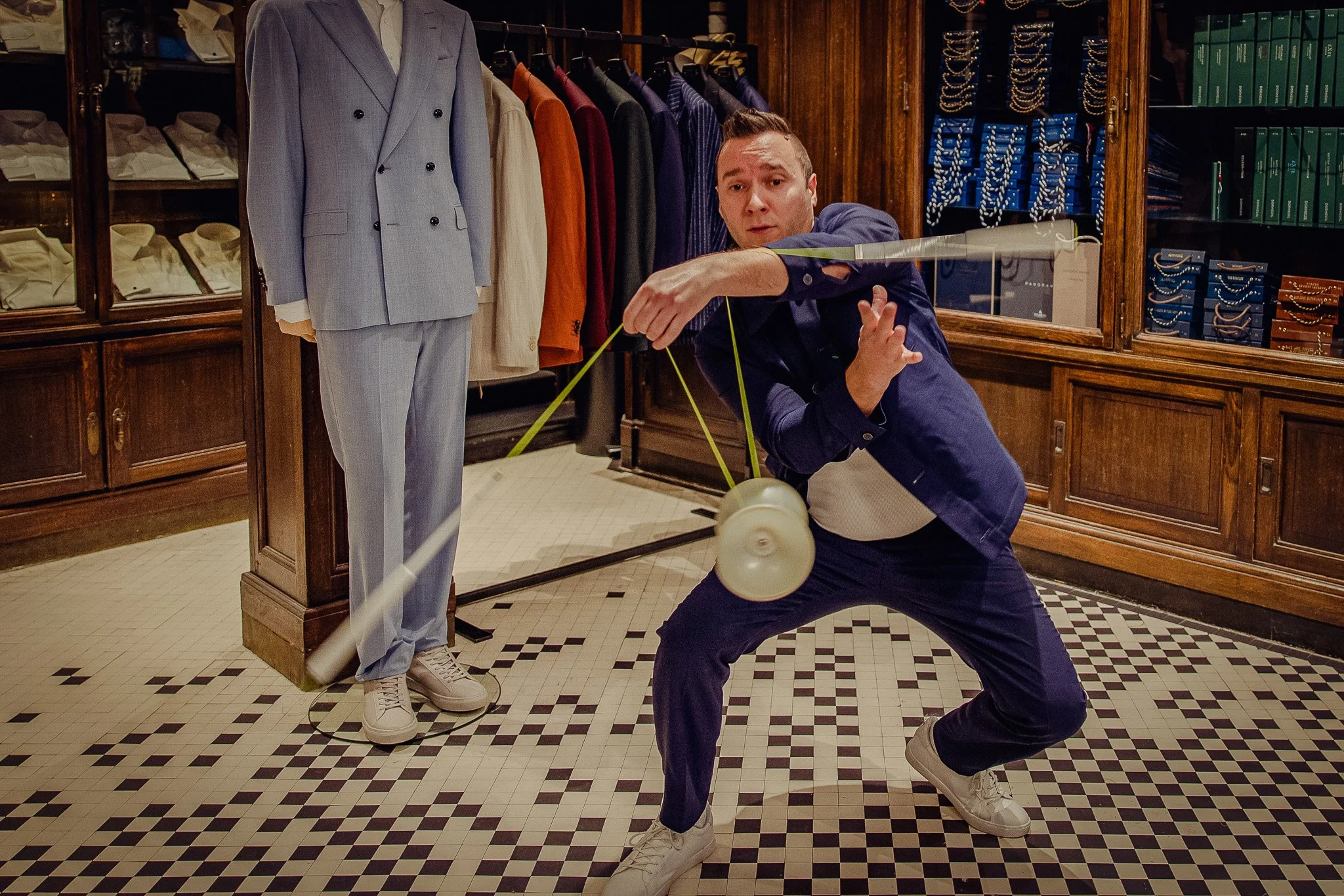 Homme en costume dans une boutique de vêtements, examines un mannequin avec un costume gris, avec des étagères de vêtements en arrière-plan.