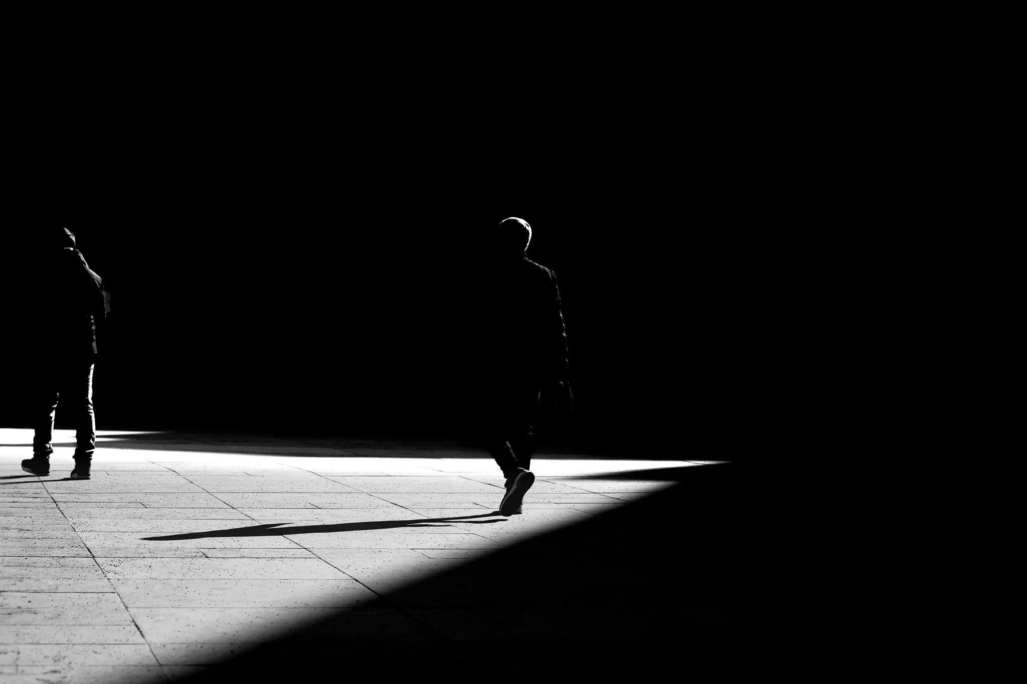 Silhouettes de trois personnes marchant dans une zone éclairée par la lumière, avec un fond sombre.