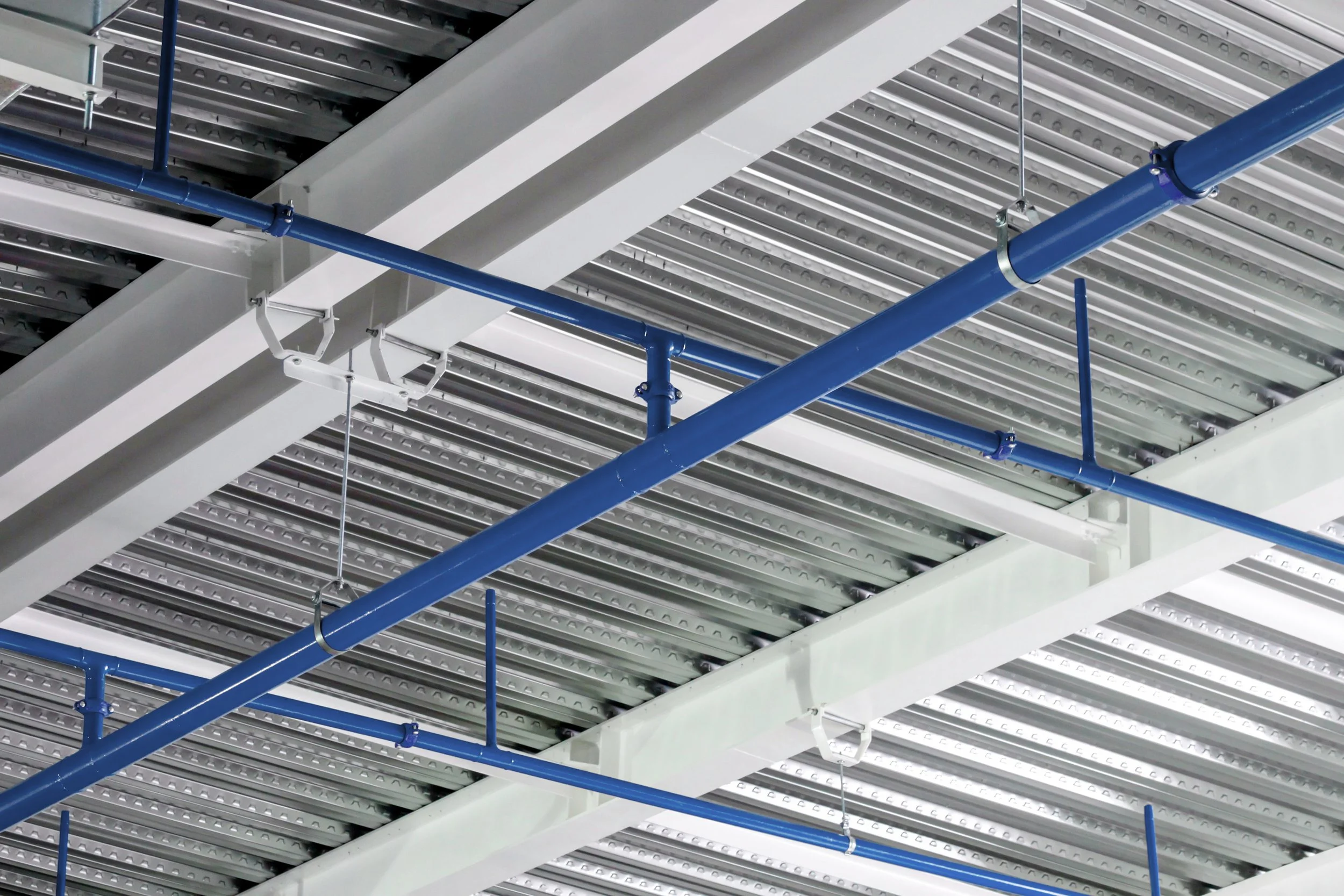 Ceiling with metal beams, white structural supports, and blue piping, indicating an industrial or commercial setting.