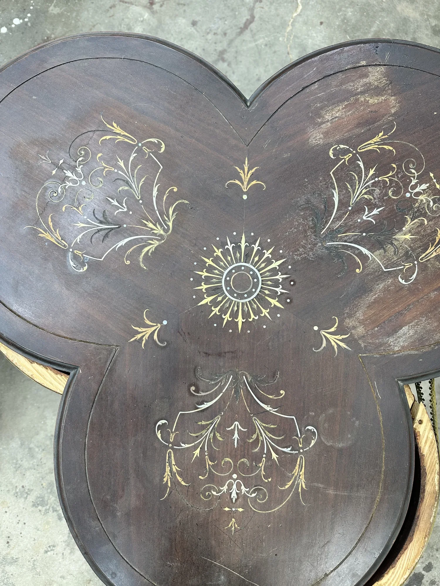 Inlaid top of a trefoil guéridon before restoration, with sunburst and scrollwork inlay dulled by a worn, water-marked finish