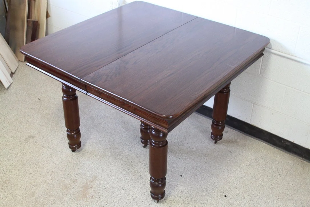 Wooden dining table with a dark finish, four rounded legs, and a rectangular top in a room with beige carpet and white walls.